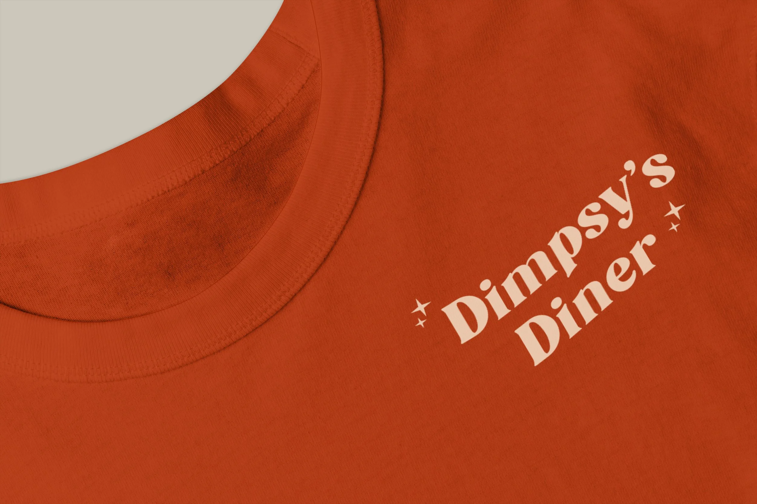 Close-up of an orange T-shirt with white text that reads 'Dimpsy's Diner' and small star icons.