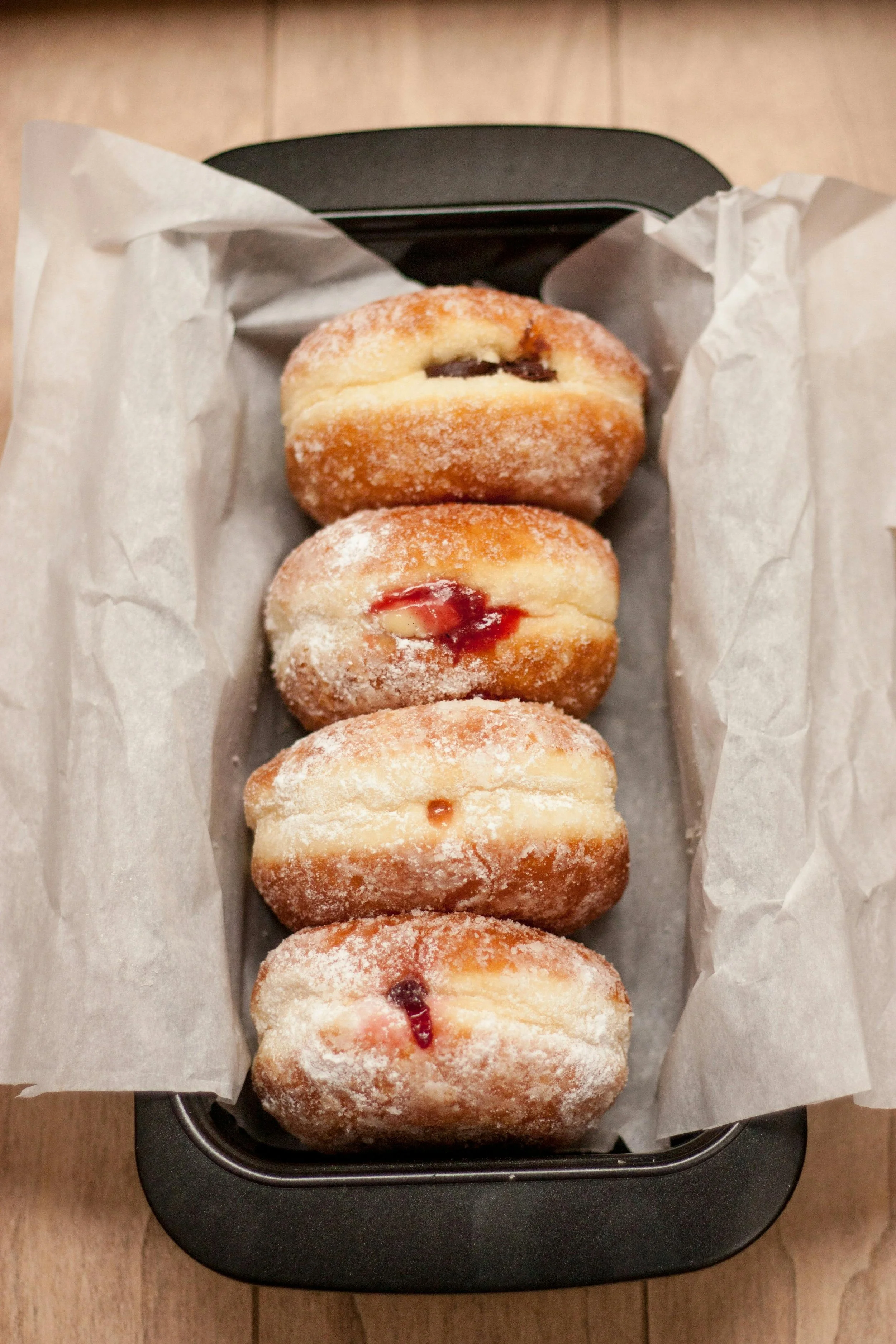 Four sugar-coated donuts with fruit filling in a black baking dish lined with parchment paper.