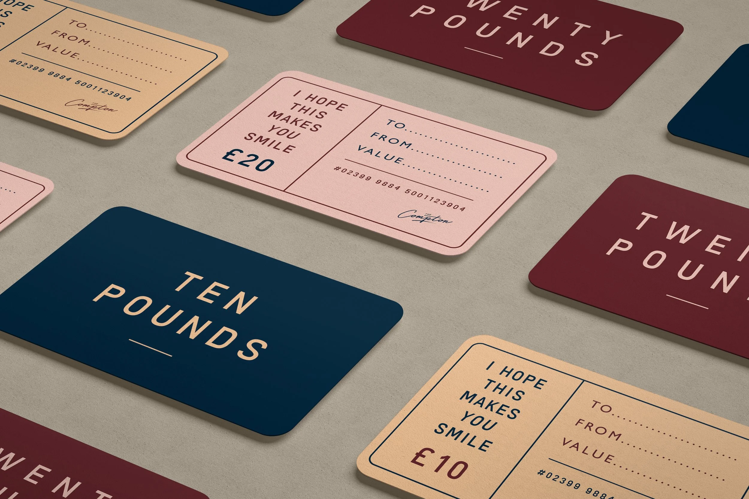 A collection of gift cards on a beige surface, including pink, navy, and burgundy cards with various monetary values and messages like 'I HOPE THIS MAKES YOU SMILE' and amounts of £10, £20, and £10.