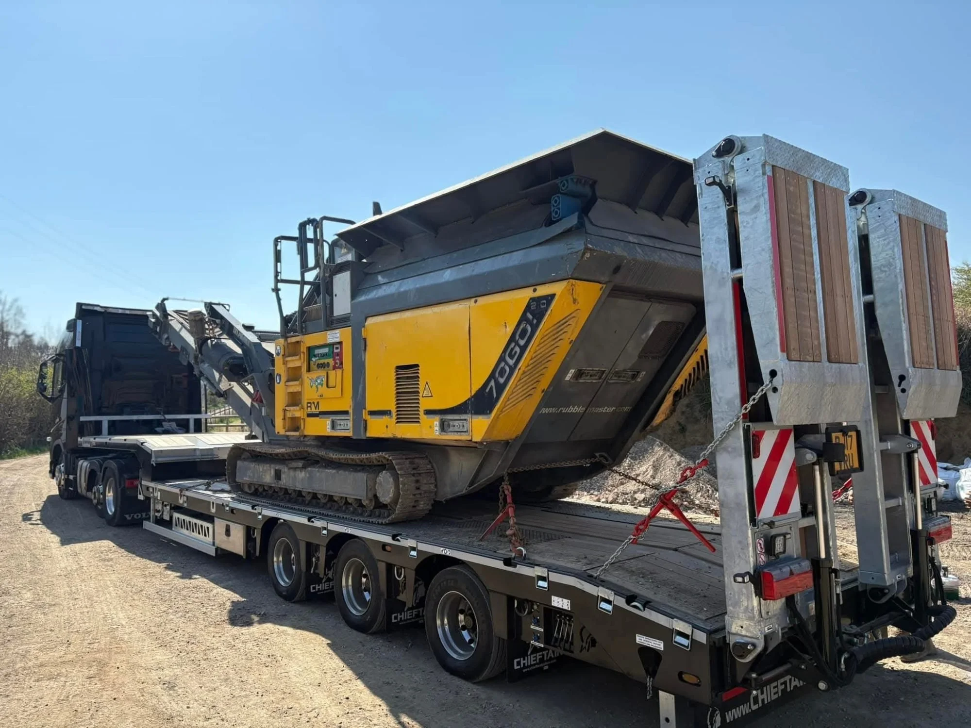 A yellow and black rubber tracked mini excavator on a flatbed truck trailer.