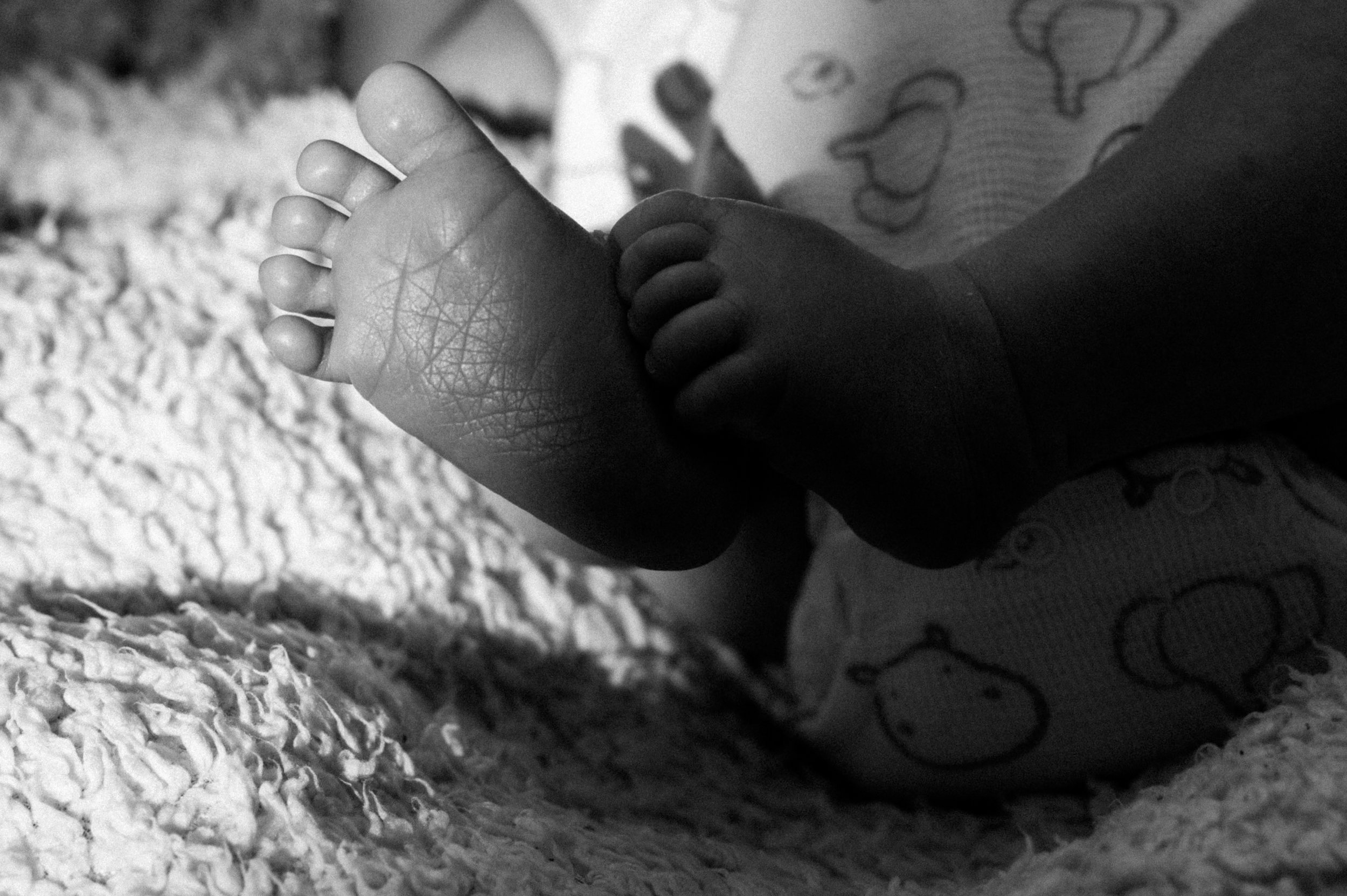 Photo en noir et blanc d'une petite main de bébé avec des doigts potelés et une peau rugueuse, posée sur une surface douce et textured, avec une autre main de bébé partiellement visible à côté.