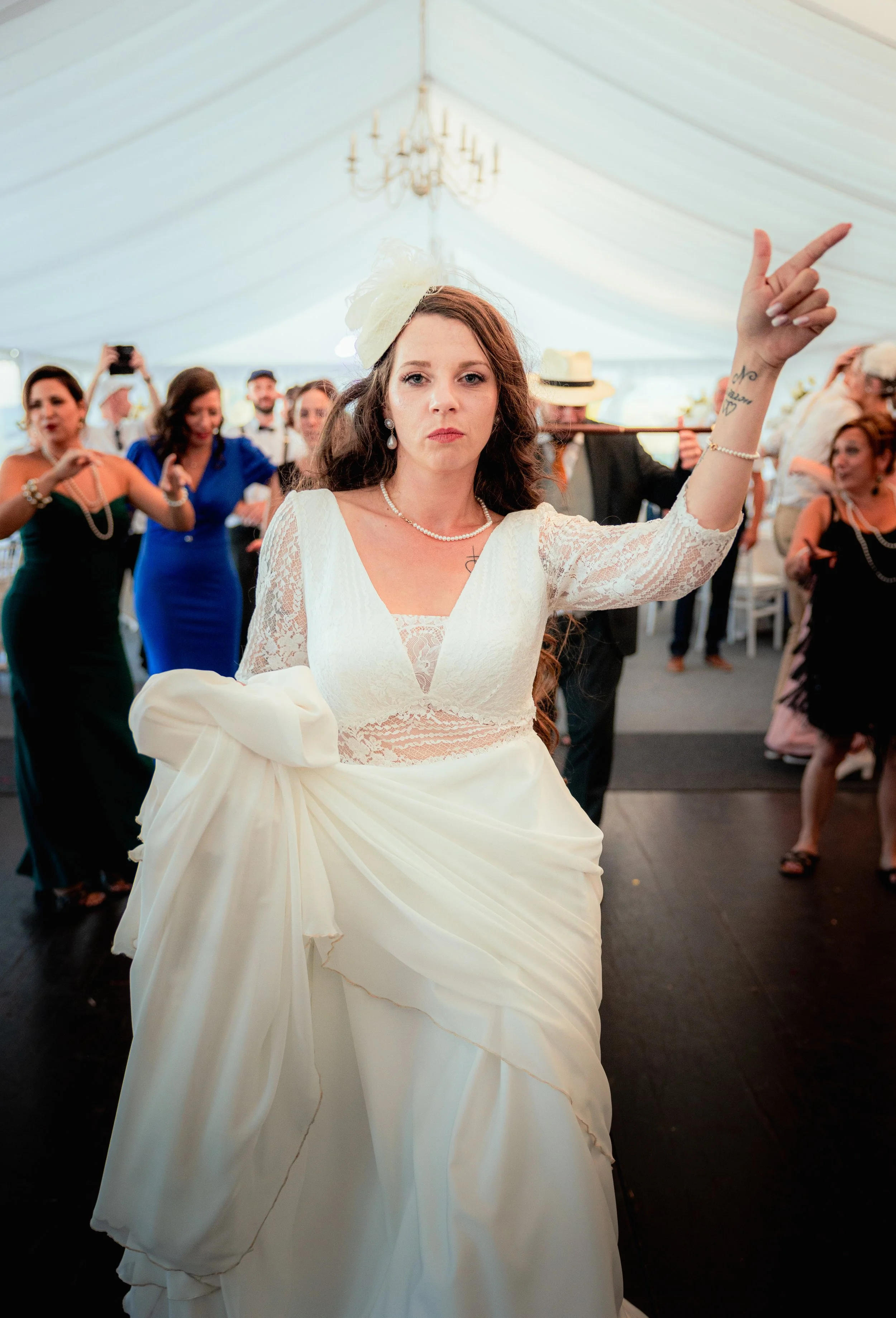 Kévin CONTI Photographe Alsace. Une femme habillée en robe de mariée lors d'une fête ou réception, entourée de plusieurs personnes en tenues élégantes dans une tente décorée, probablement à un mariage.