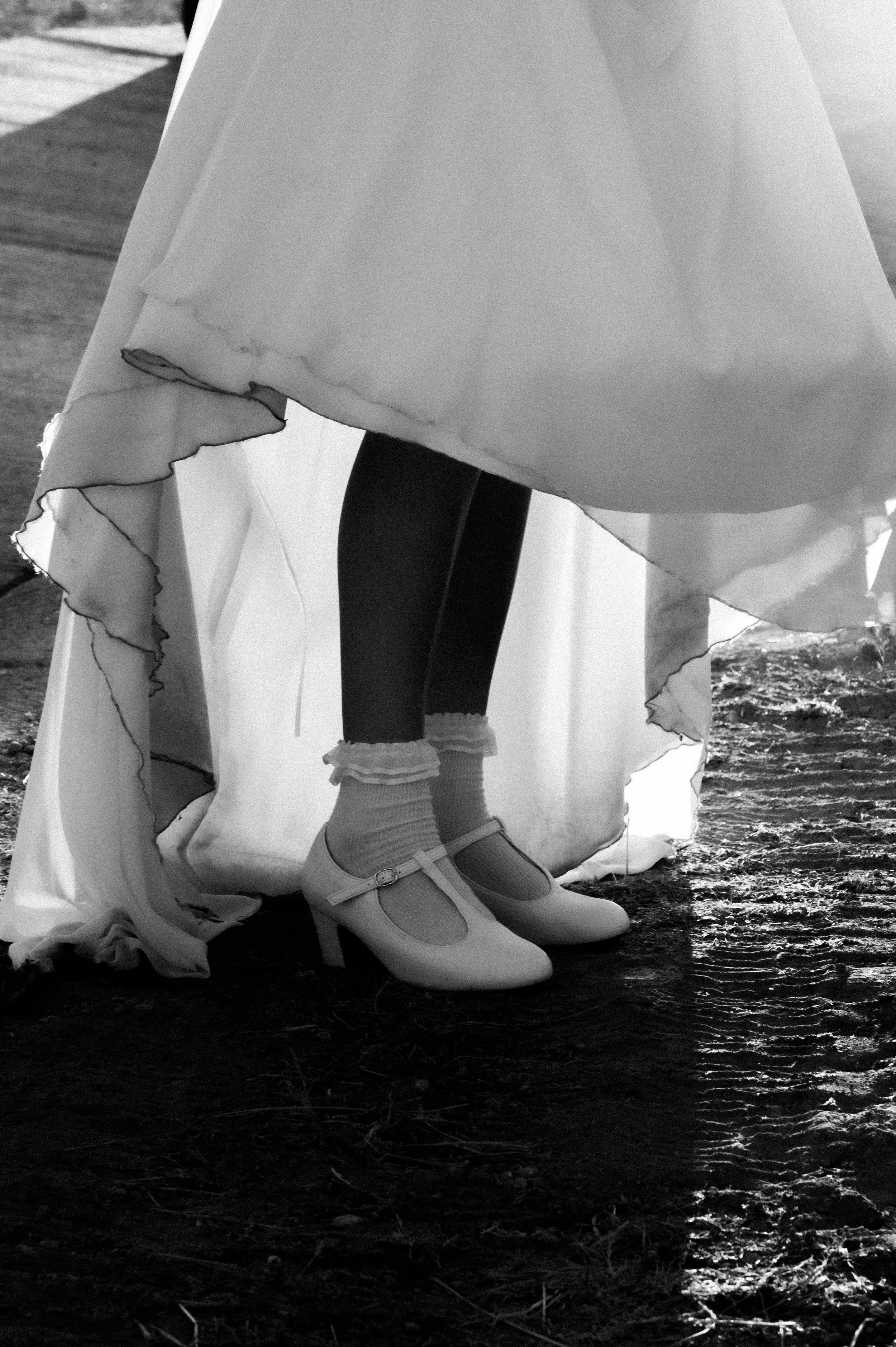 Photographie d'une mariée, au domaine du Bollenberg à Westhalten. Paire de chaussures de ballerine avec des chaussettes rayées, portée par une personne portant une robe longue. La photo est en noir et blanc. Probablement un mariage.