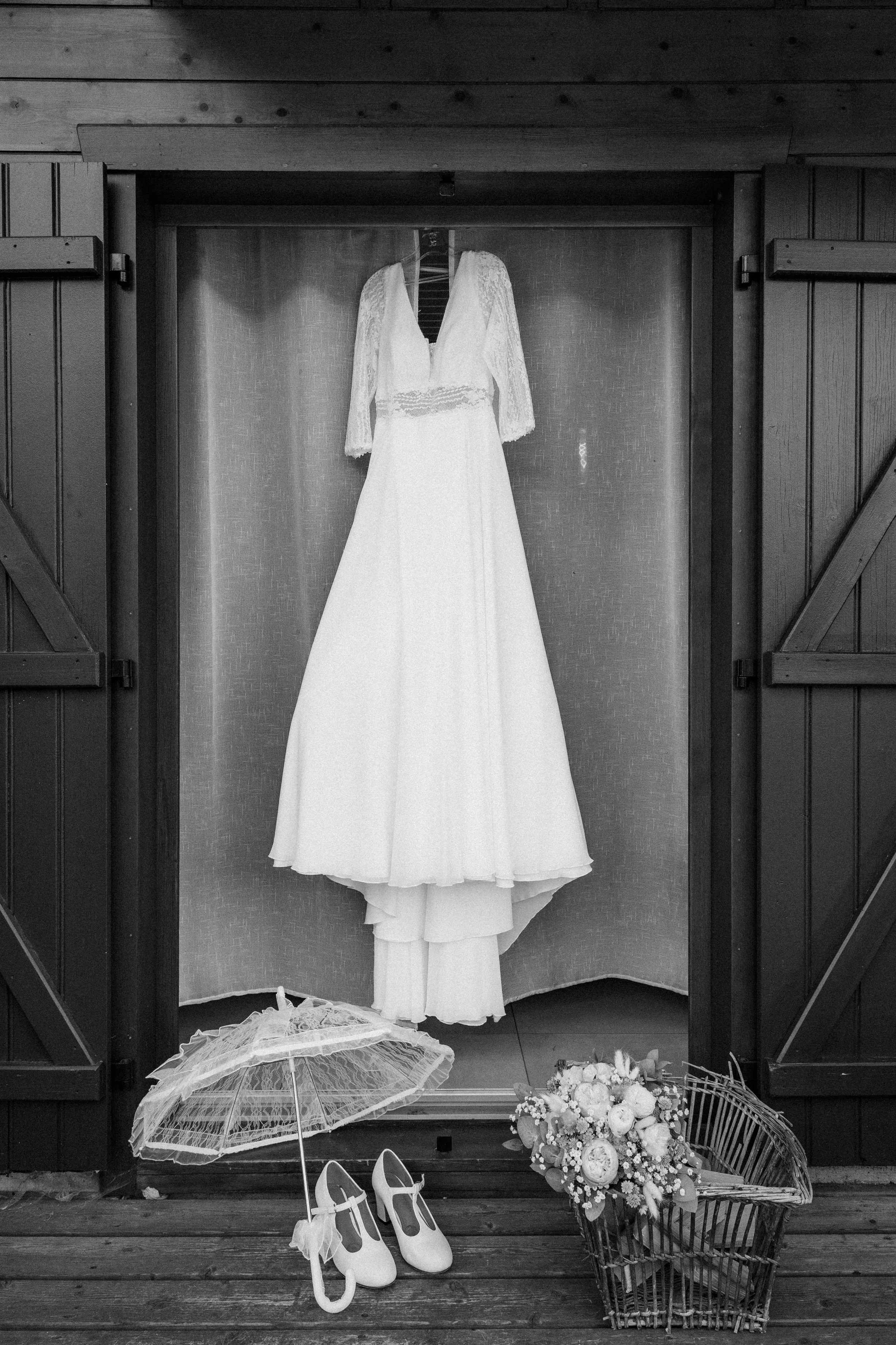 Robe de mariée blanc dans une vitrine, avec une ombrelle en dentelle, des chaussures de mariage et un bouquet de fleurs au sol.