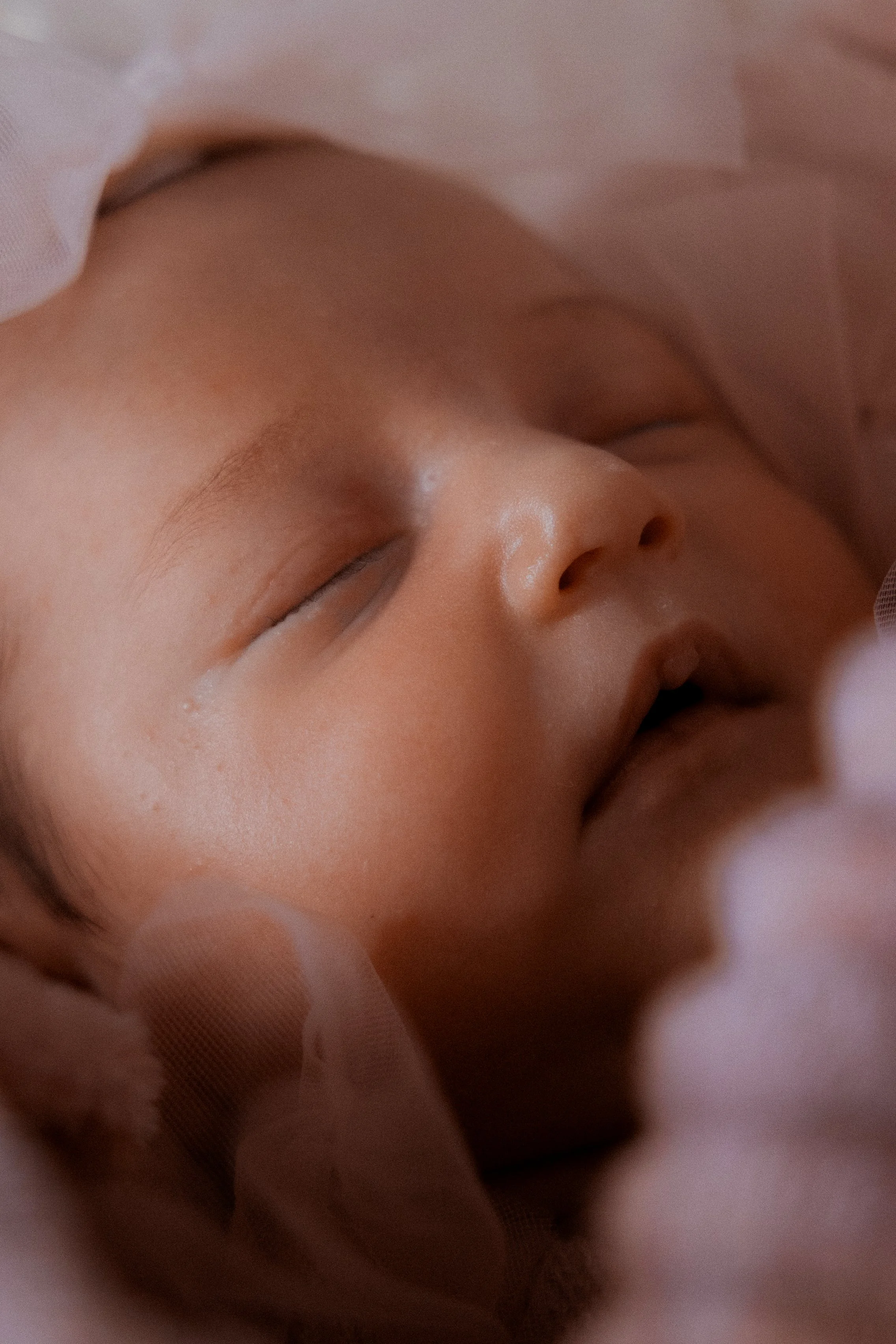 Un bébé dormant avec un visage paisible, entouré de tissus doux. Photographe de bébé et naissance en Alsace.