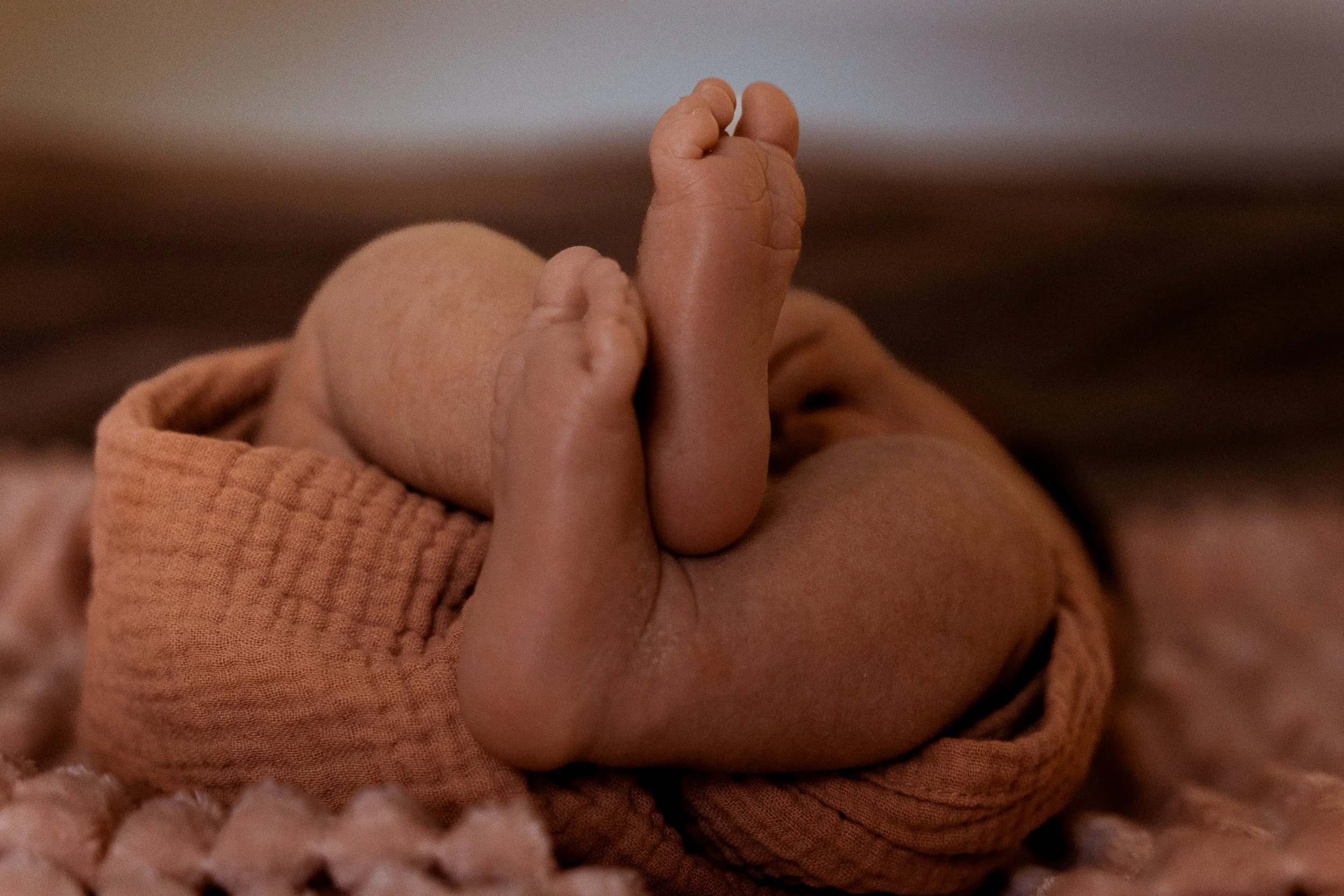 Un bébé dormant avec ses petits pieds en premier plan, portant une veille de couleur orange.