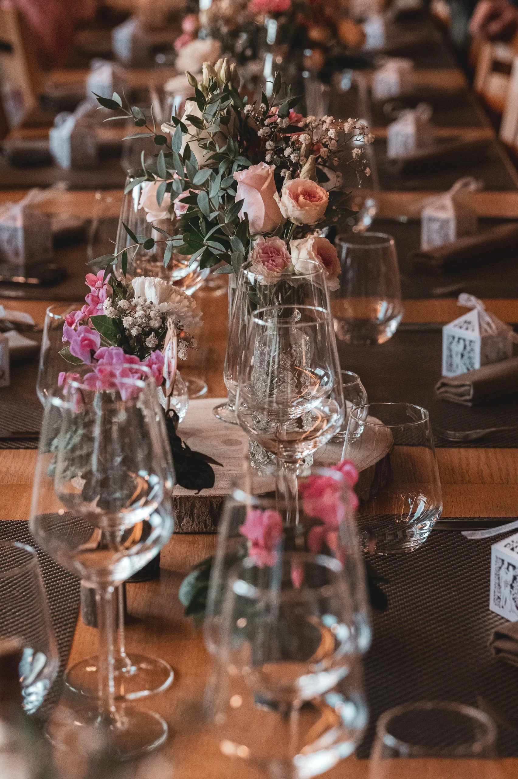Une table élégamment décorée avec des fleurs roses et blanches dans des vases en verre, avec des verres à vin et des assiettes en céramique disposés, prêt pour un repas.