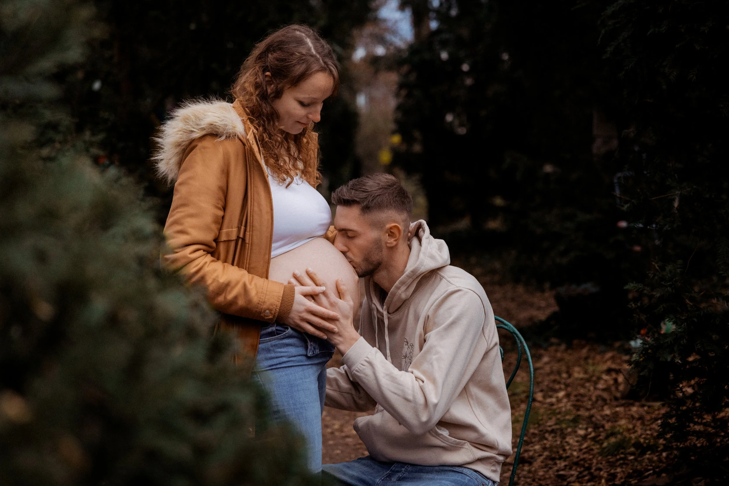 Un homme embrasse tendrement le ventre d'une femme enceinte, dans un parc, lors d'une séance photo d'automne.
