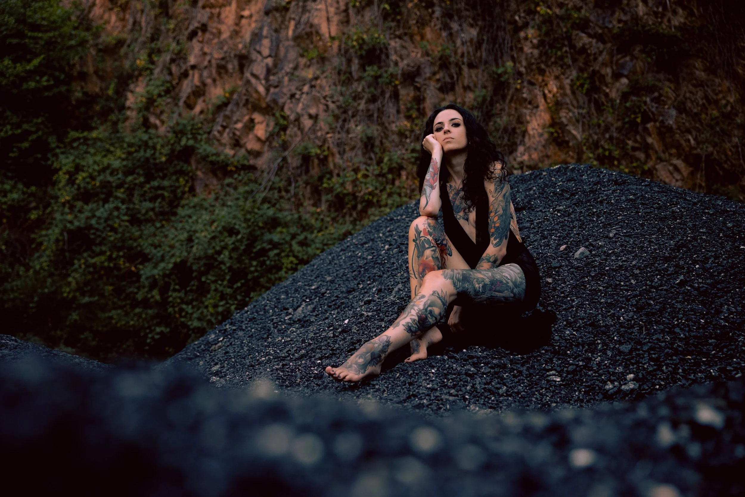 Femme tatouée assise sur un tas de cendres noires dans un paysage rocheux