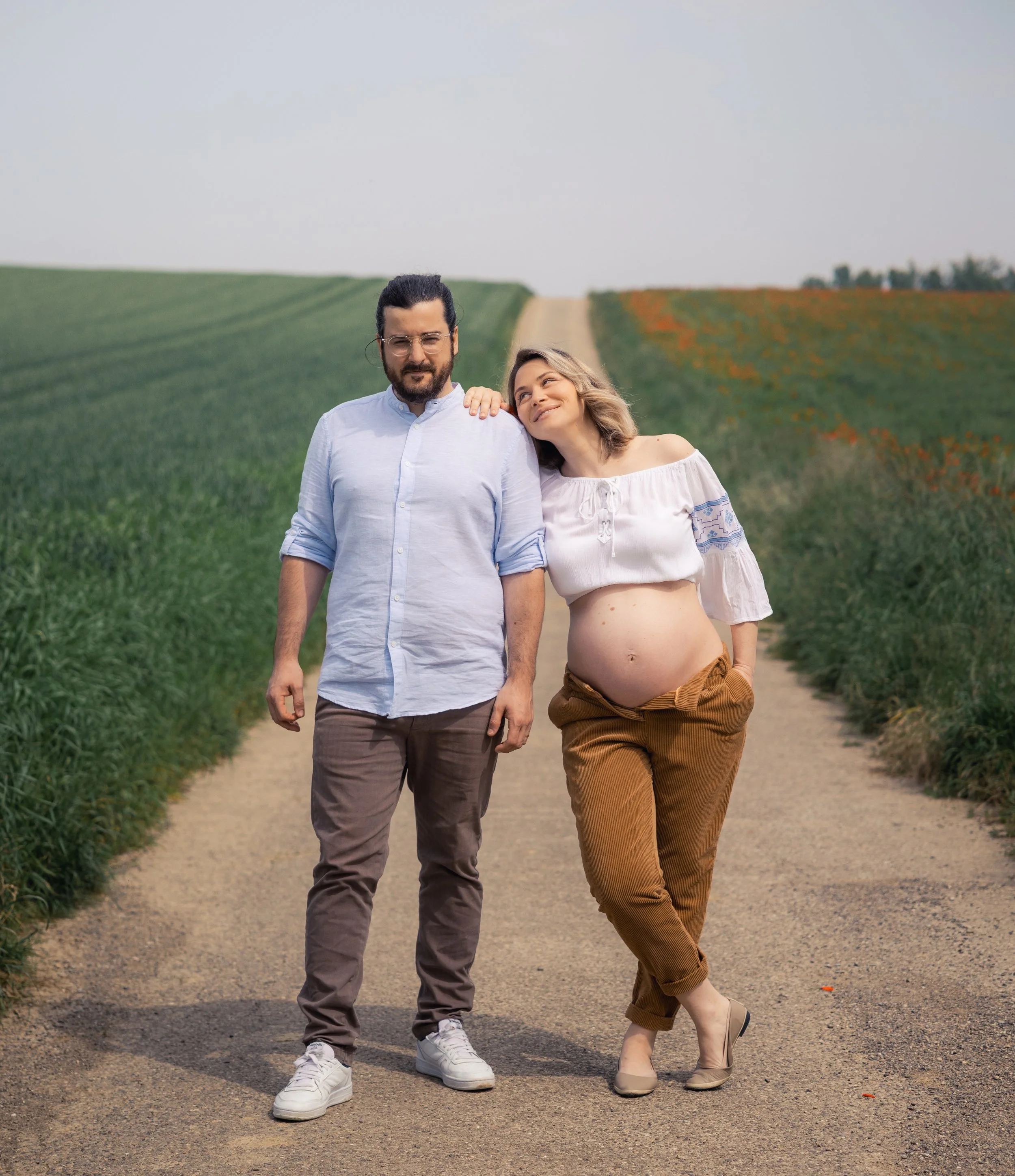 Un couple marchant dans un chemin rural, la femme est enceinte, elle est en train de se reposer sa main sur l'épaule de l'homme.