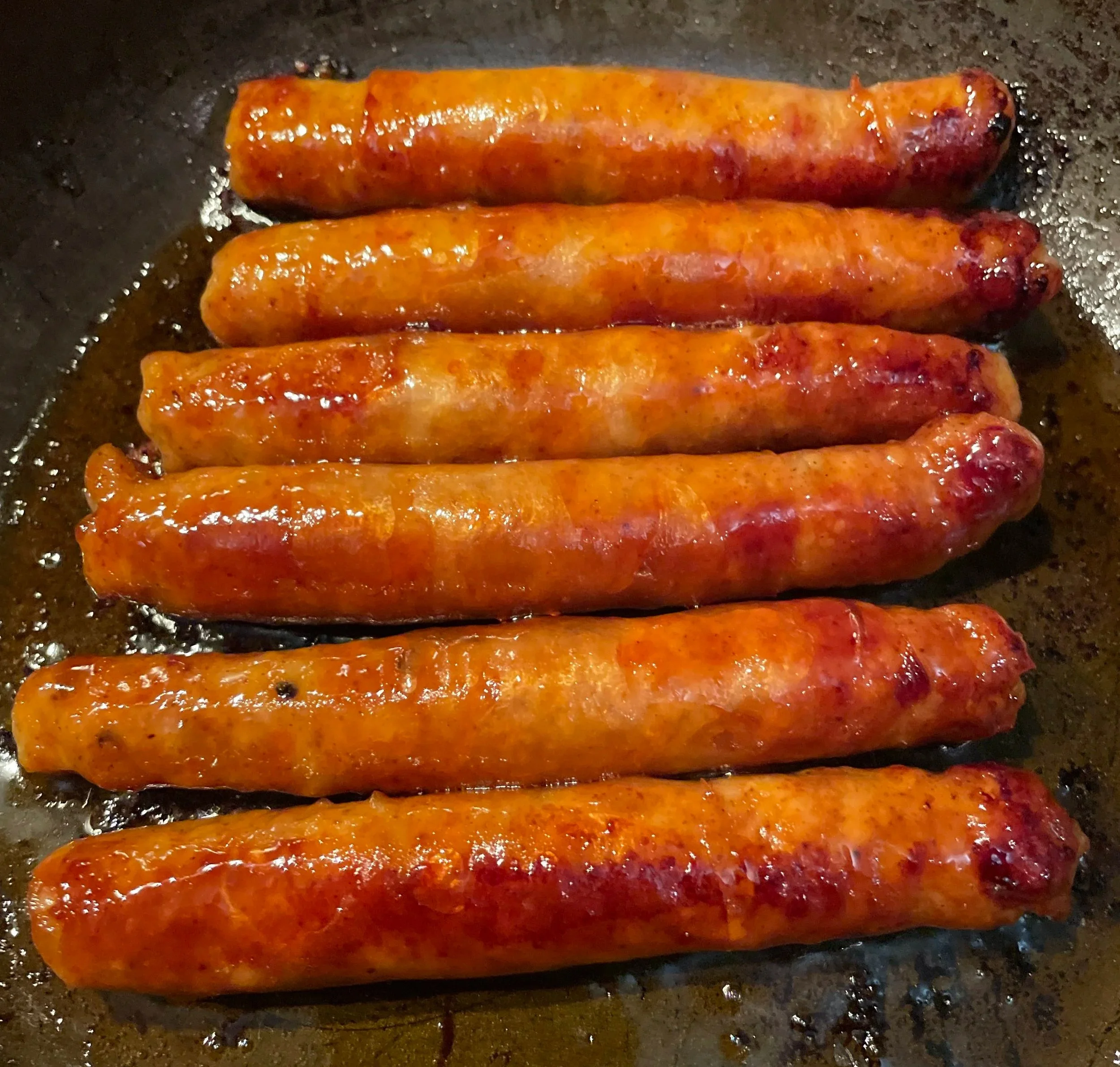 Several cooked sausage links in a pan with some oil.