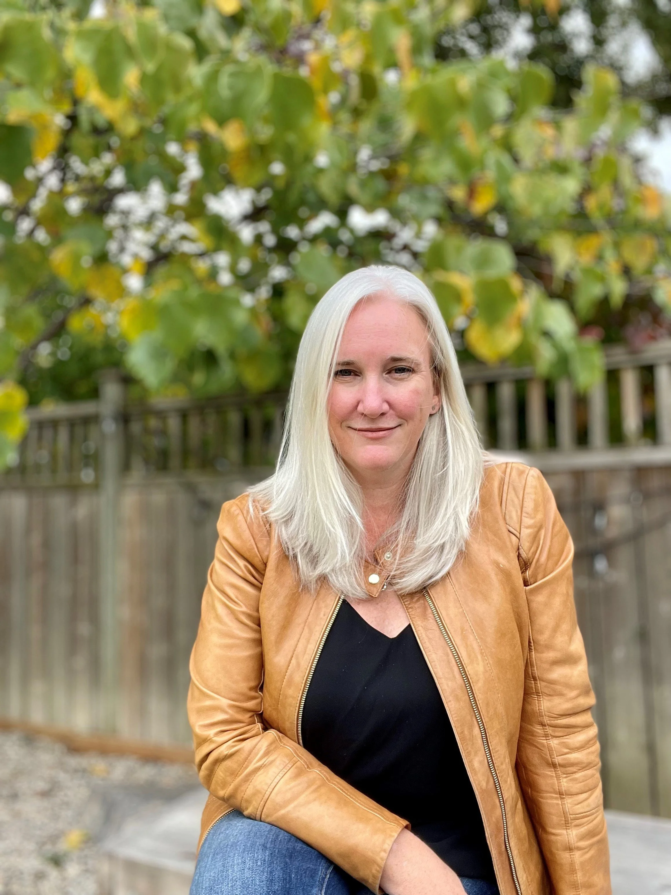Andrea Tsuji in her backyard, wearing a caramel jacket and black top.