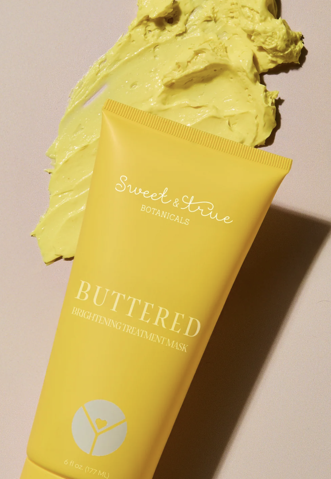 Yellow tube of Sweed & Youve Botanicals Buttered Brightening Treatment Mask with some yellow mask spread on a flat surface.