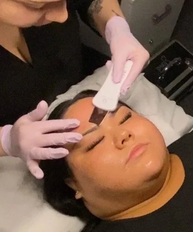 Skincare professional using a handheld facial treatment device on a client’s forehead