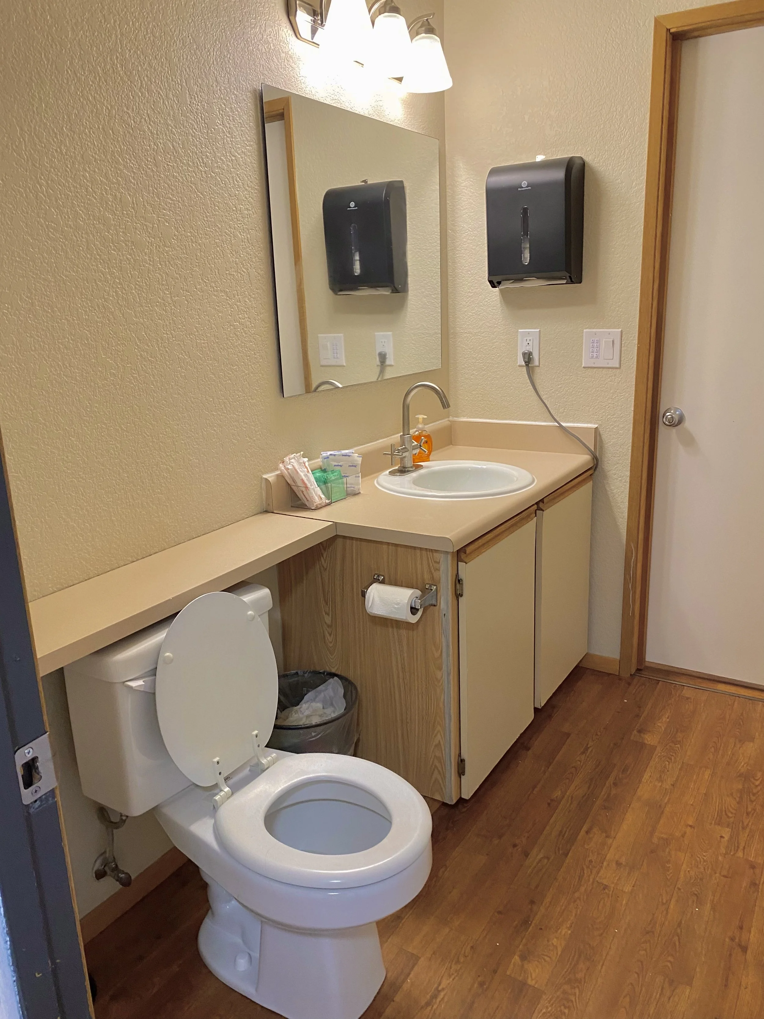 a cozy bathroom with a toilet, mirror, and hand towel dispenser with free hygiene products and soap