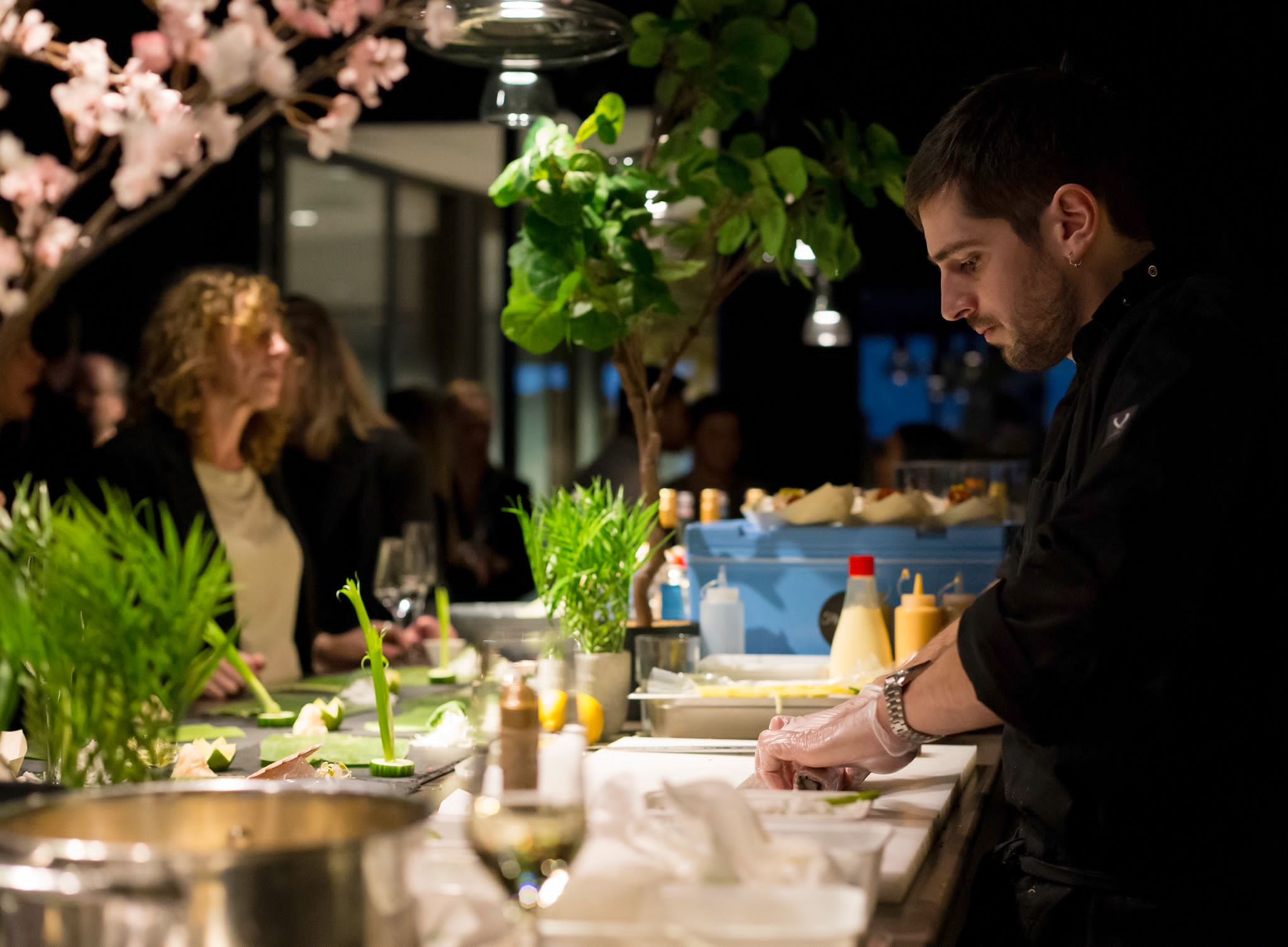 A variety of sushi rolls and sashimi on leaf-shaped platters and a central dish, decorated with flowers and petals, with soy sauce and ginger on the side.