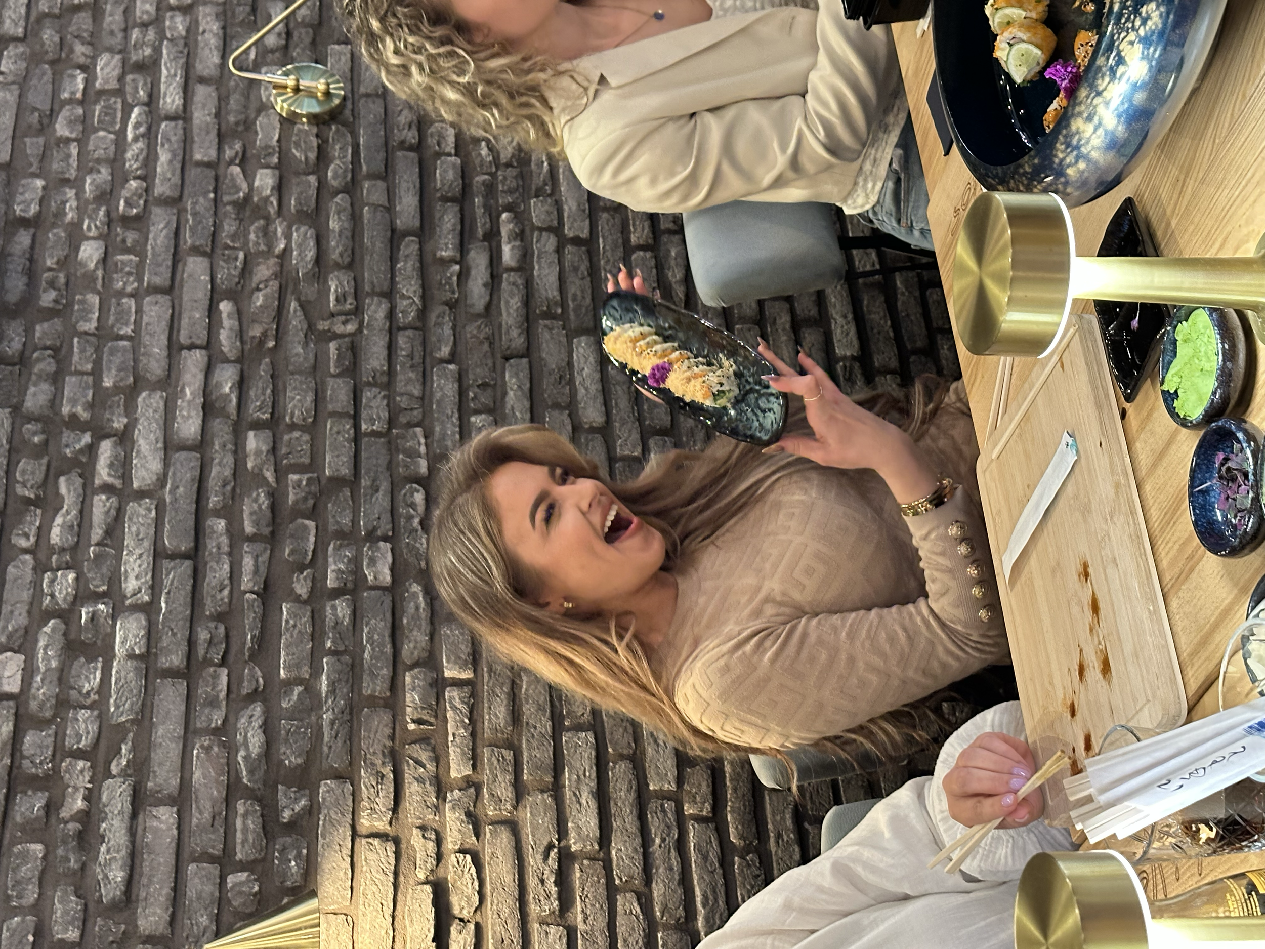 Person using chopsticks to pick up sushi rolls at a restaurant table.