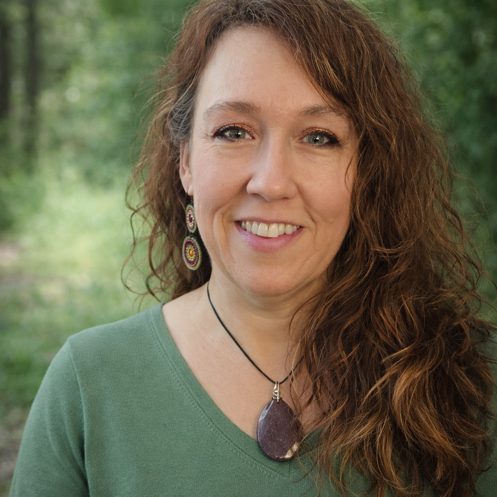 A woman with curly brown hair, wearing earrings and a black choker with a large purple pendant, smiling outdoors with trees in the background.