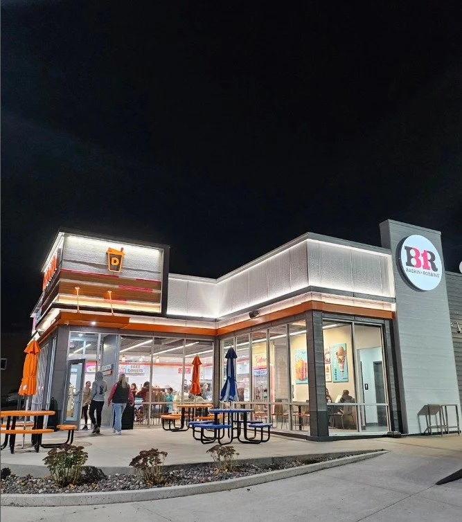 A Baskin Robbins ice cream shop at night with customers inside and outside seating.