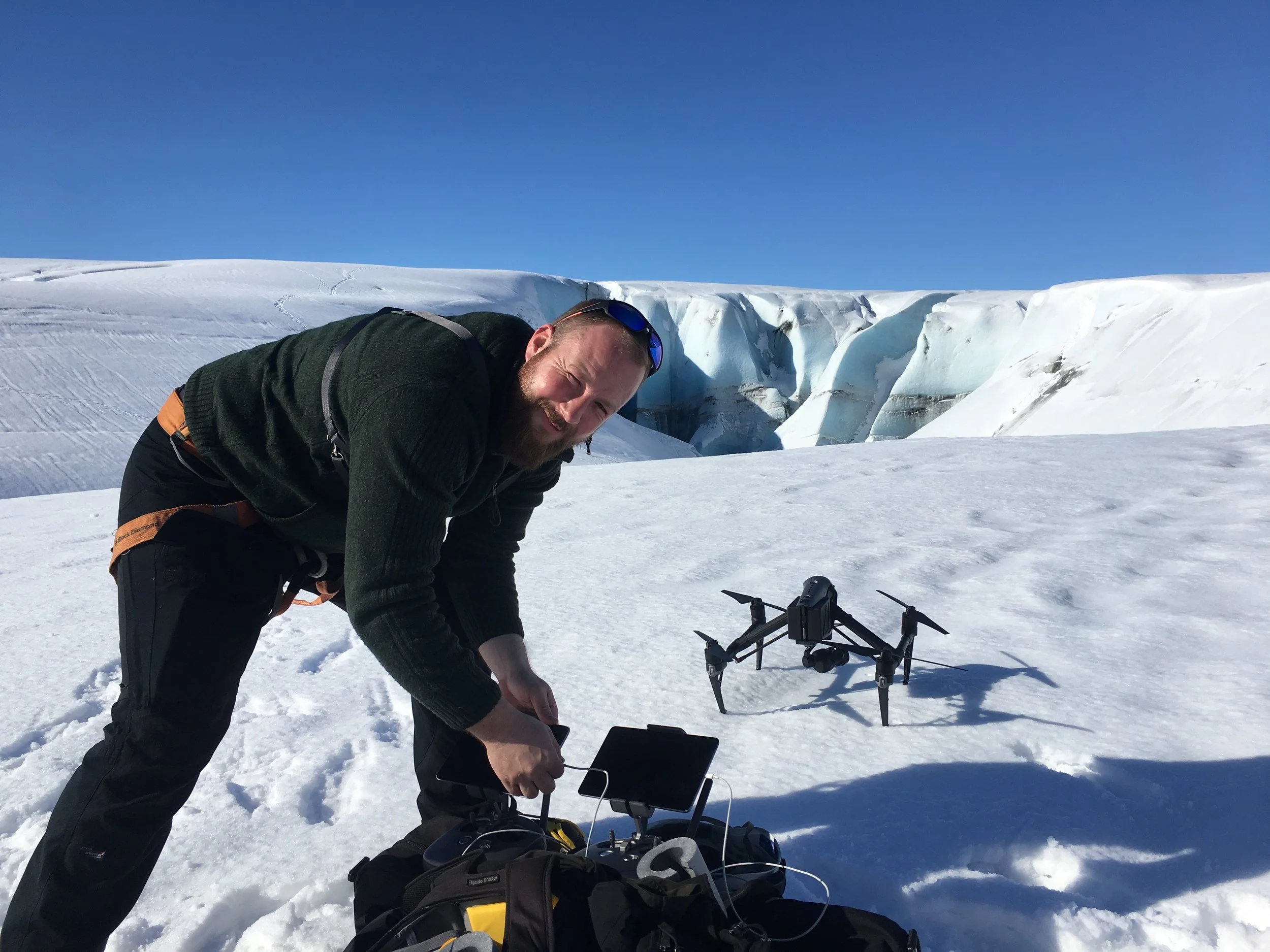 Ein Mann arbeitet mit einer Drohne in einer verschneiten Eislandschaft unter klarem blauen Himmel.