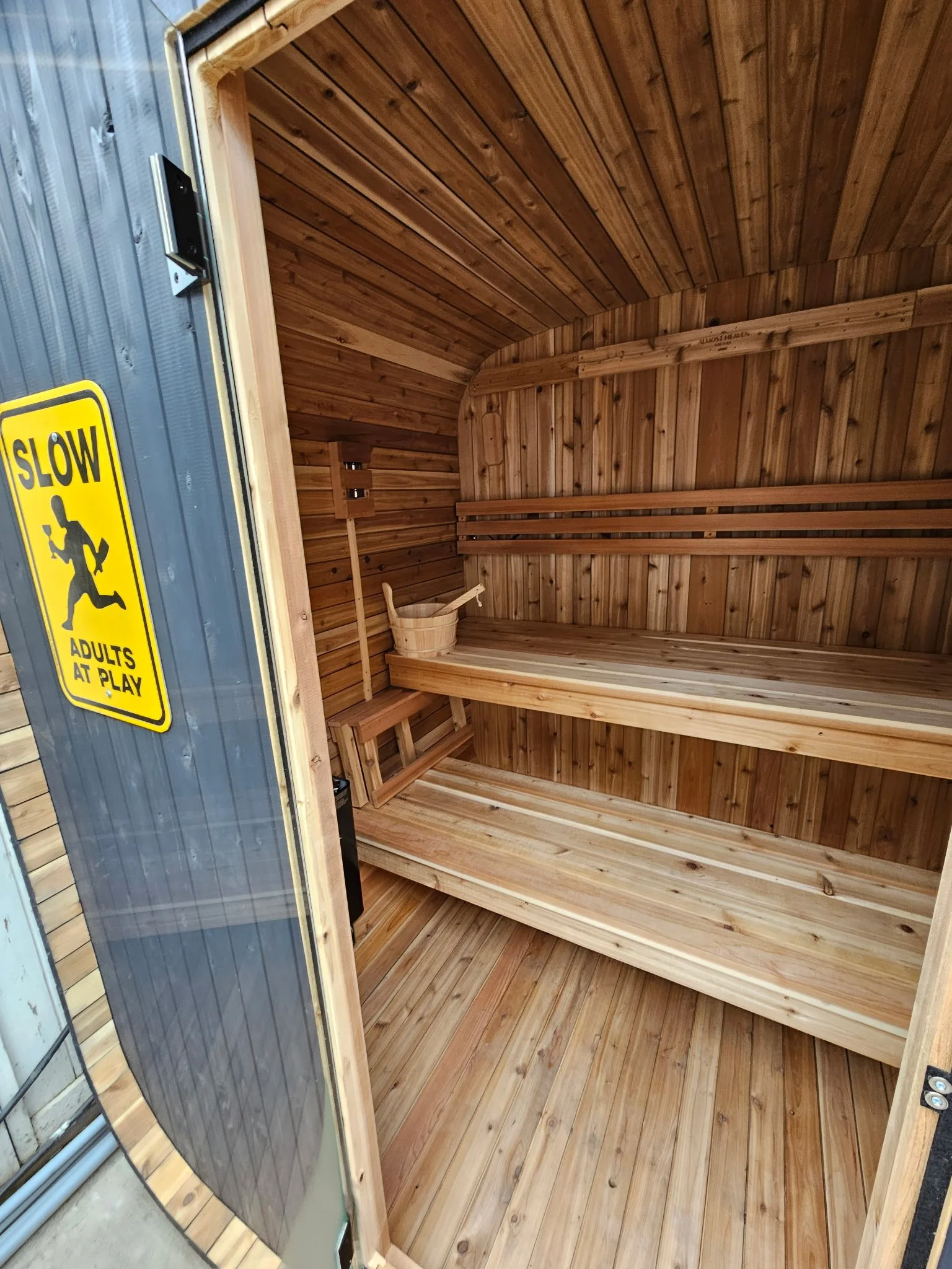Empty wooden sauna with benches and a bucket inside.