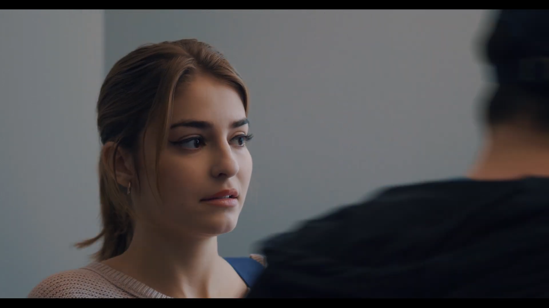 A young woman with short brown hair and light makeup looking at another person with only part of their shoulder and back visible.