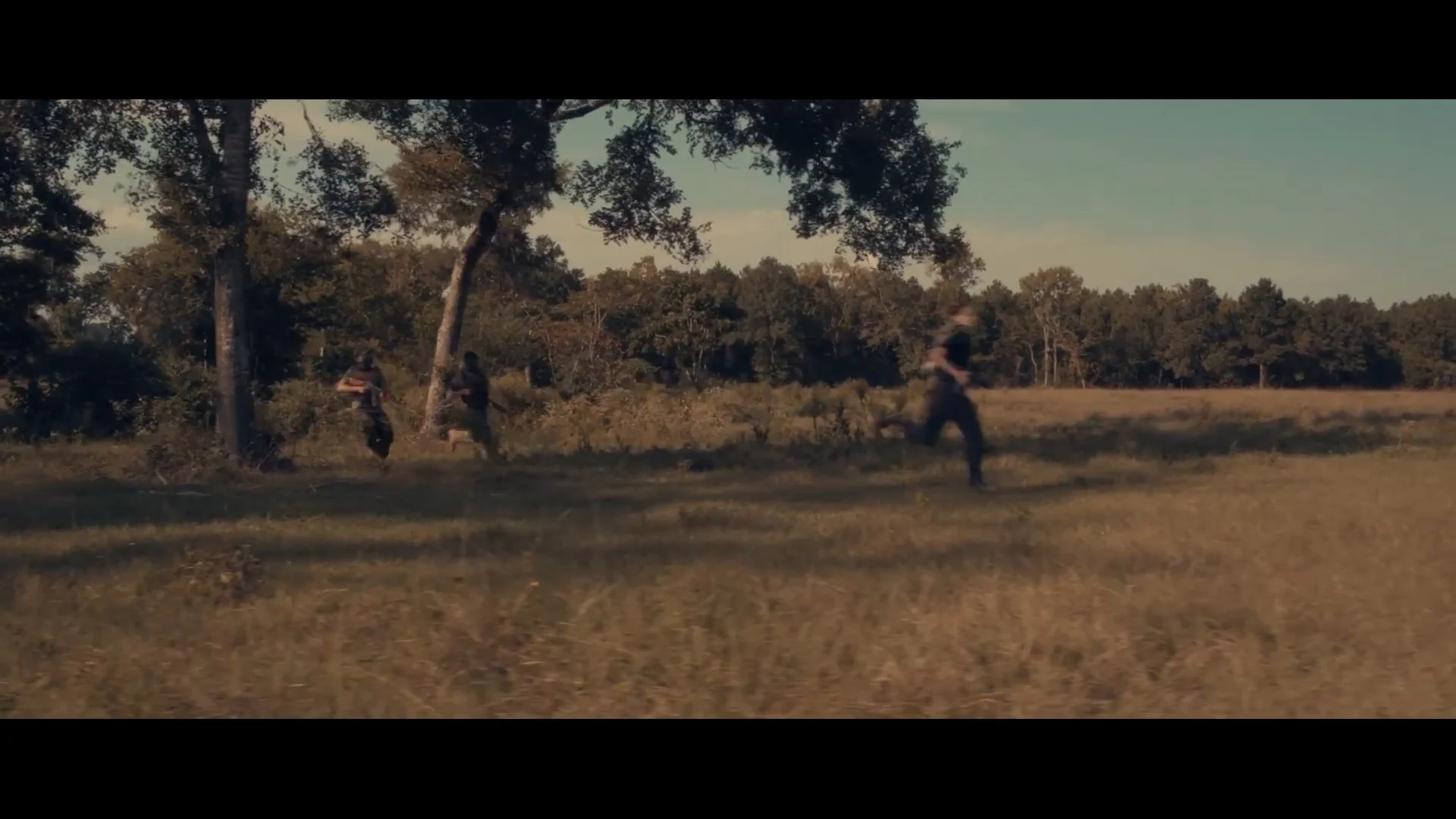 Four people running through a grassy field with trees in the background during daytime.