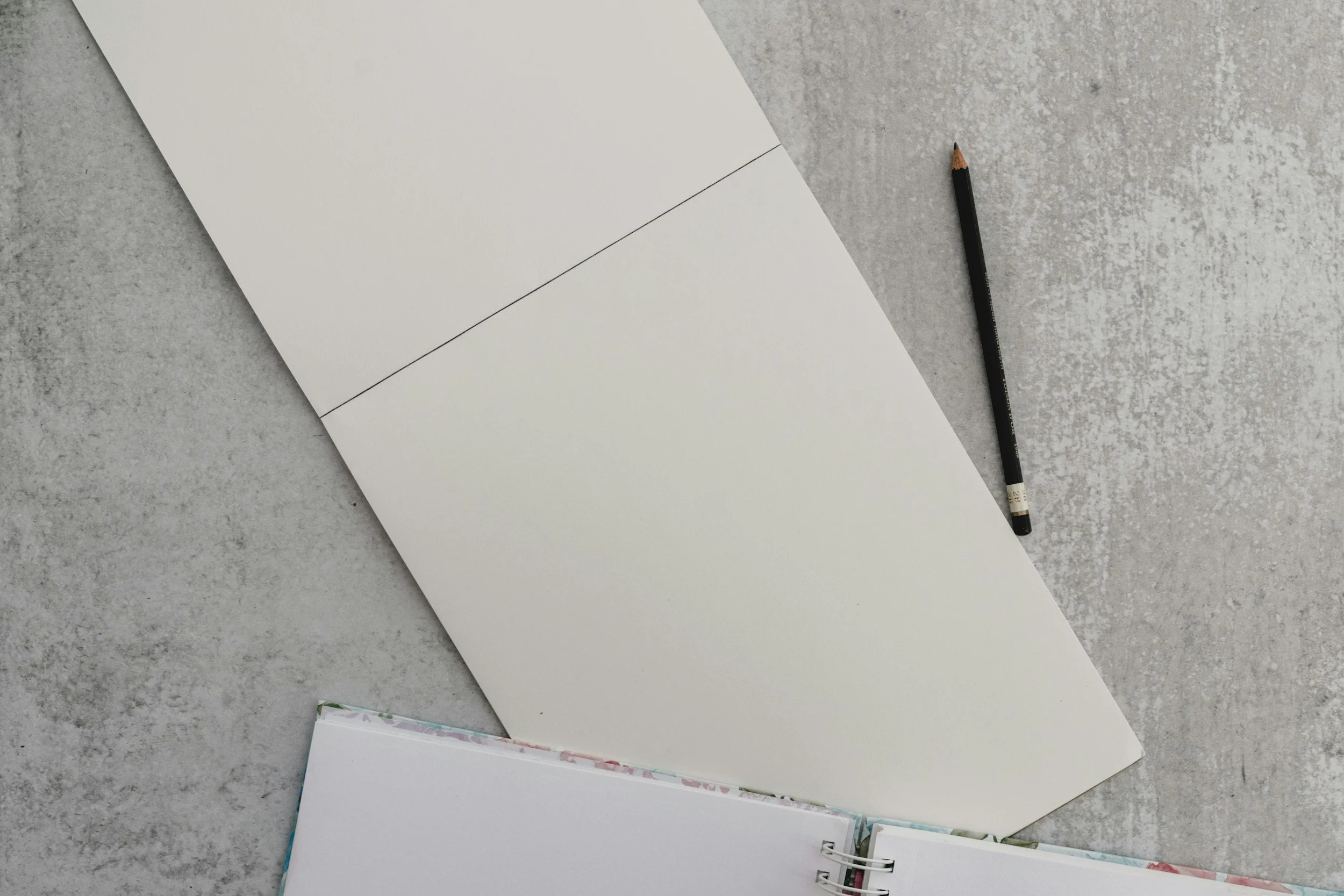 Open spiral-bound notebook with blank pages on a gray surface, with a black pencil nearby.