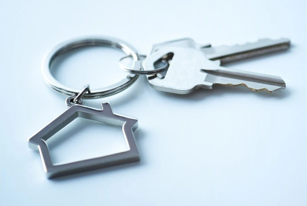 A set of silver keys with house-shaped and blank keychain charms on a light blue background.