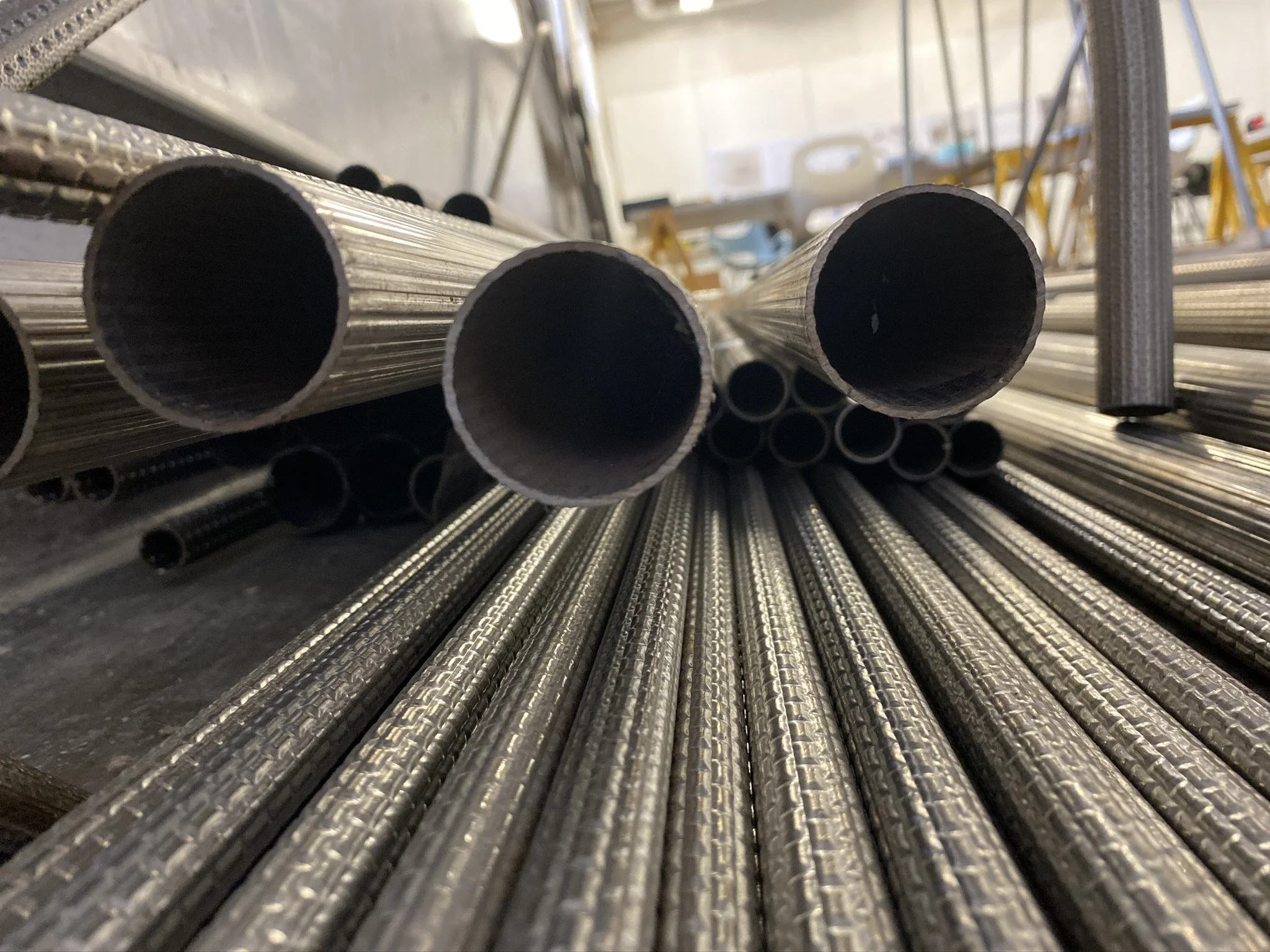 Stacked metal pipes with a reflective, textured surface on a construction or storage rack.