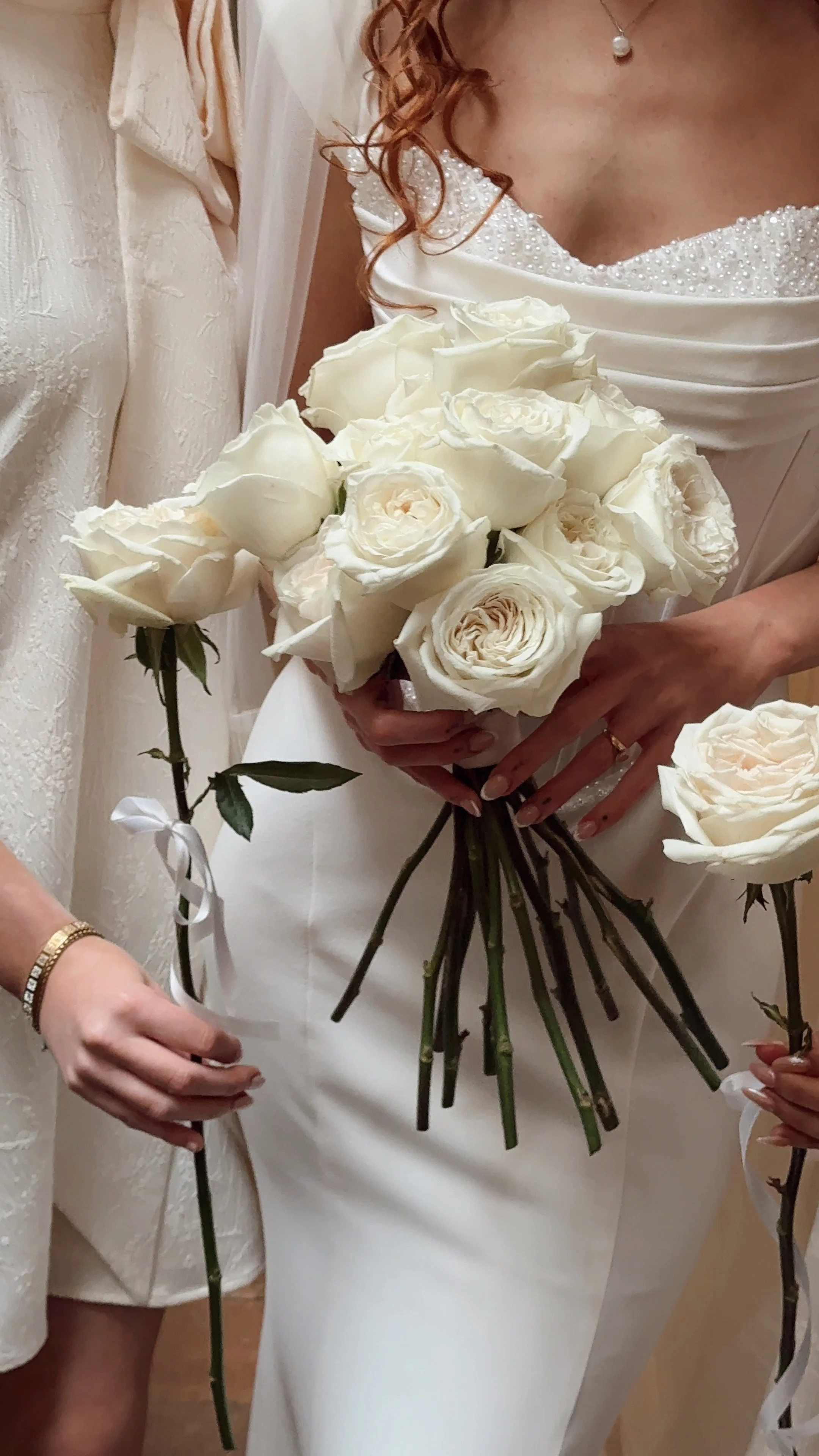 Close-up of a bride in a white wedding dress holding a bouquet of white roses.