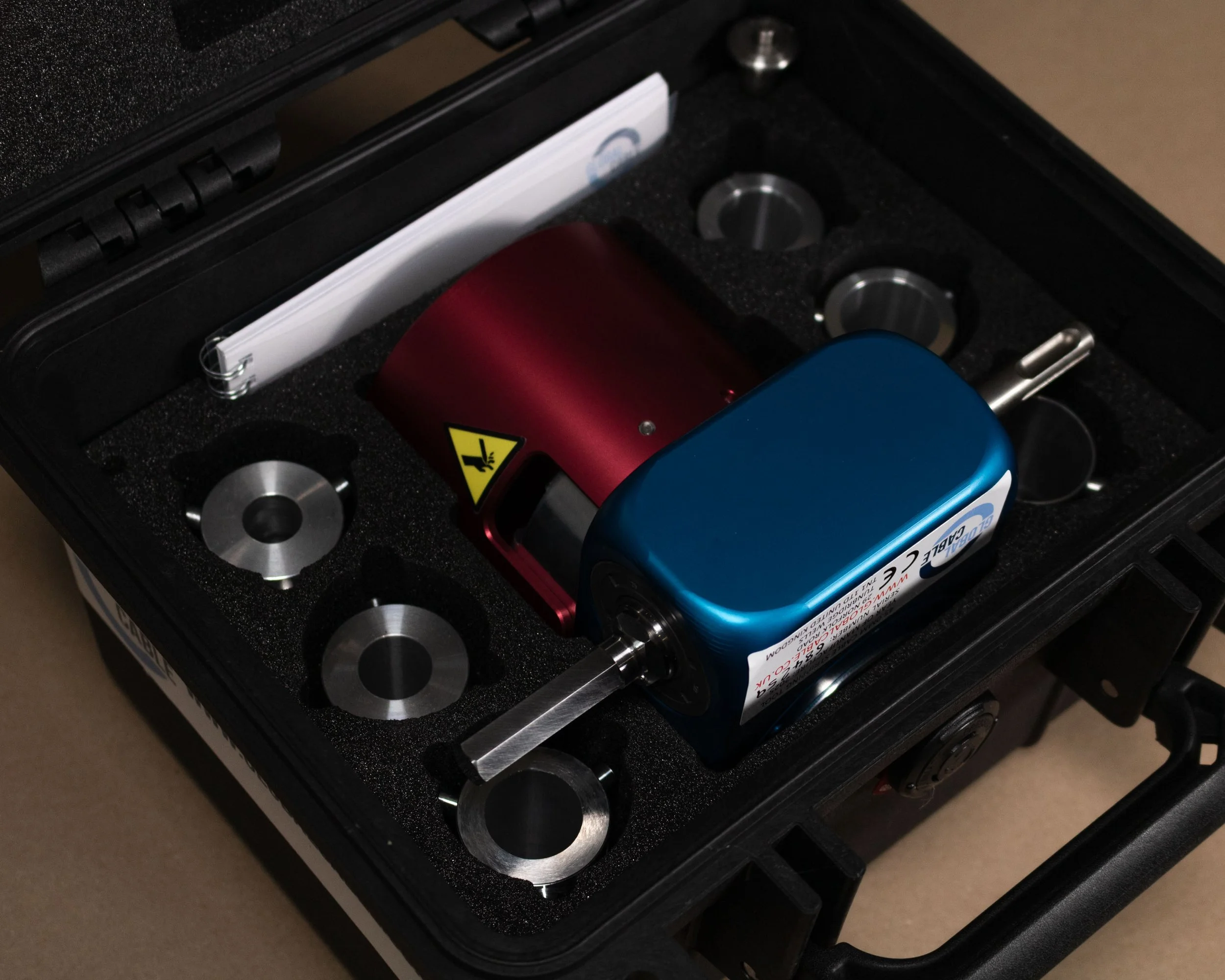 A black case with foam padding holding a red and blue handheld device and four metal circular components.