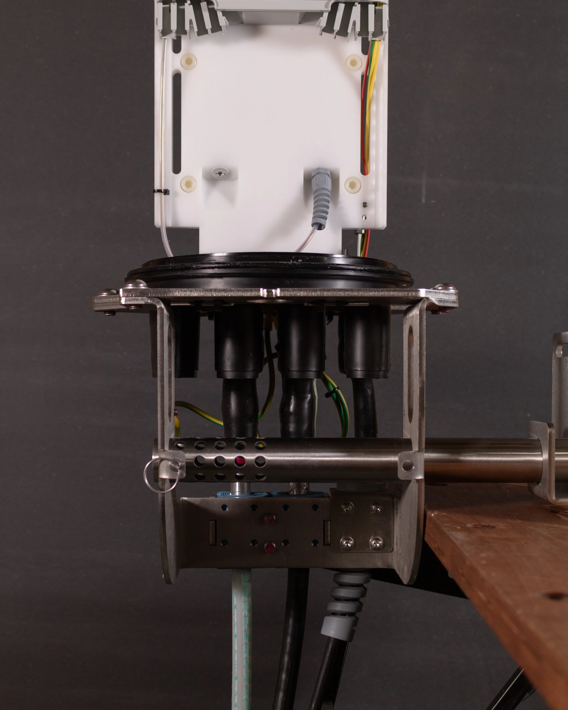 Close-up view of a mechanical or robotic device with black cables, wires, and metal components mounted on a wooden surface.