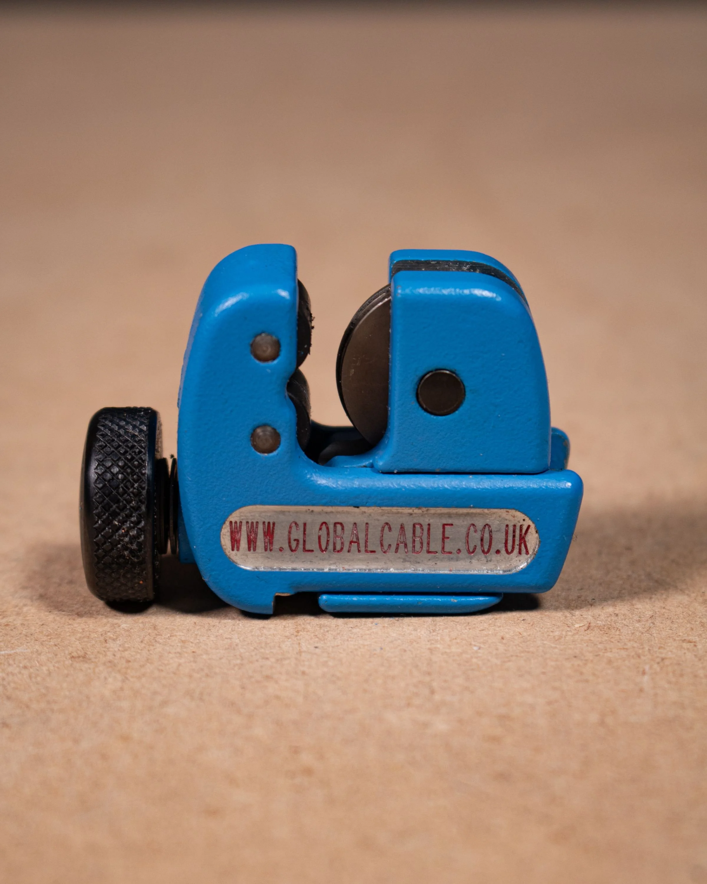 A blue adjustable wire stripping tool with black knobs and a label that reads 'www.globalcable.co.uk' on a brown surface.