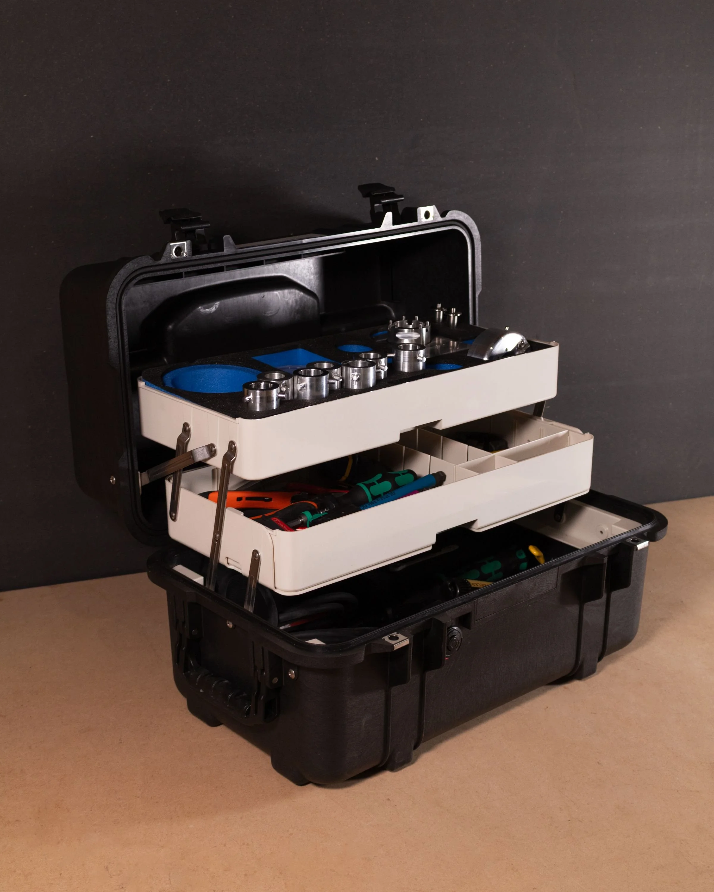 A black and white toolbox with tools and equipment inside, open on a beige surface against a dark background.