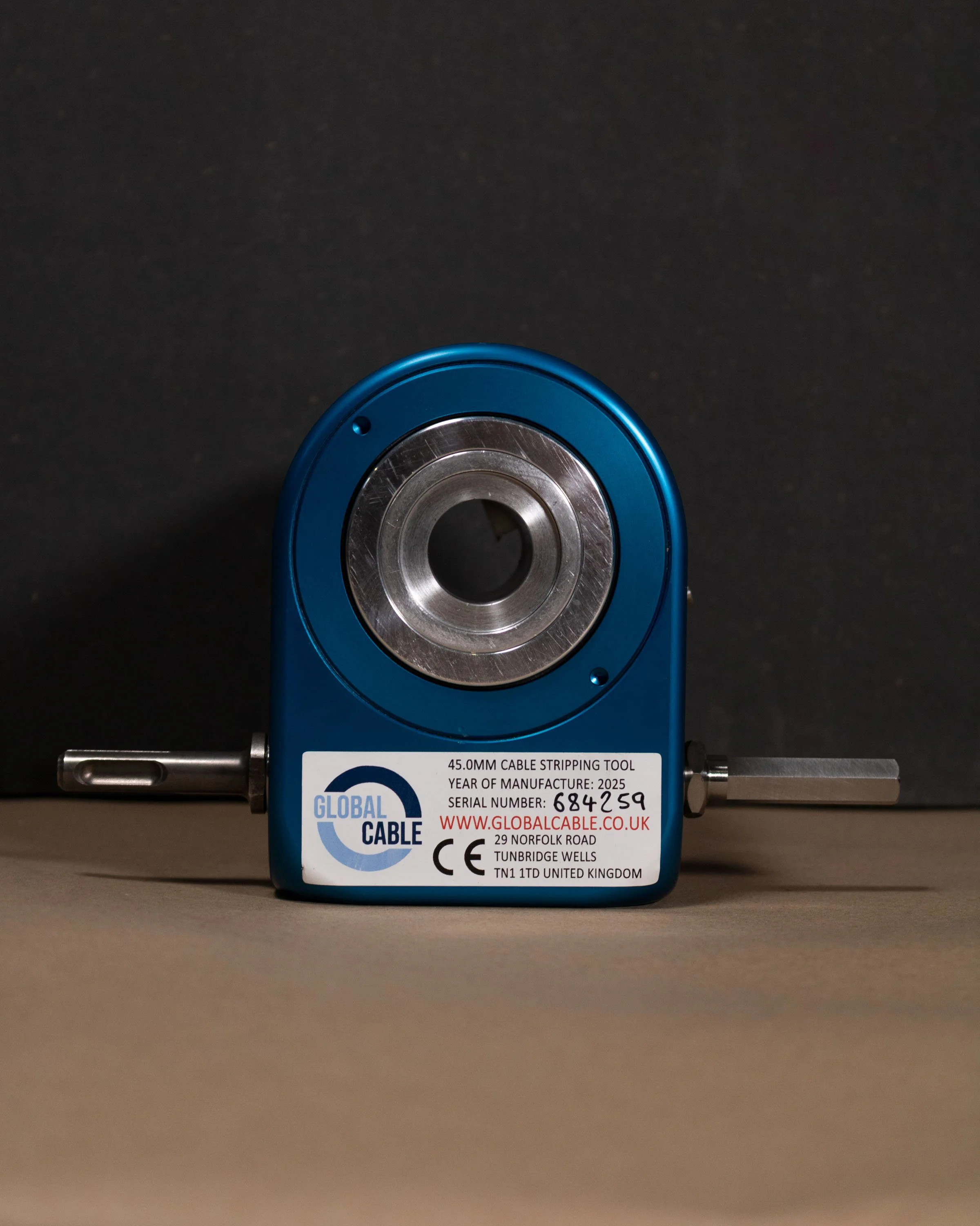 A blue cable stripping tool with metal handles and a central cutting blade, placed on a flat surface against a dark background.