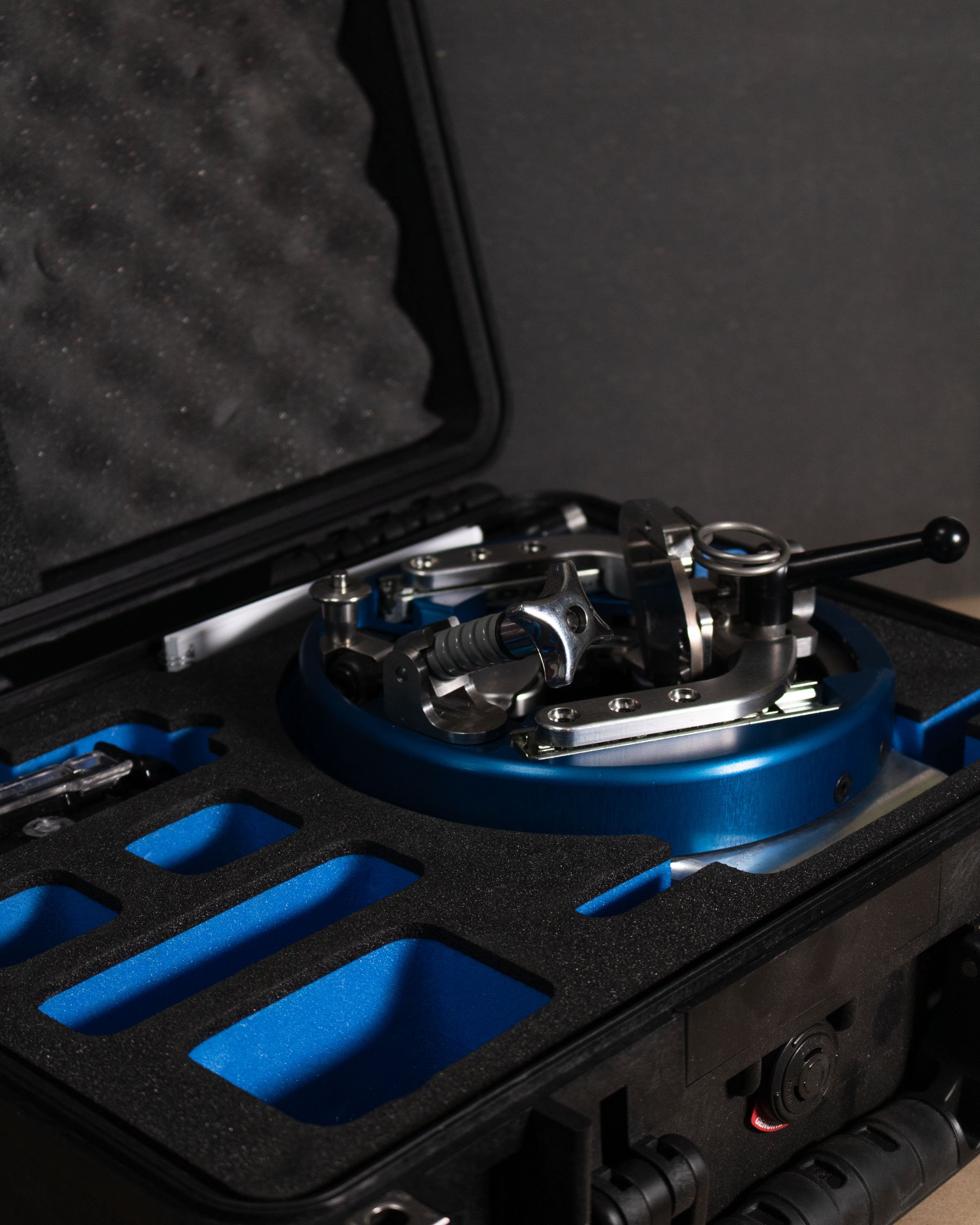 A metal turntable with various mechanical parts inside a black hard carrying case with a foam insert.