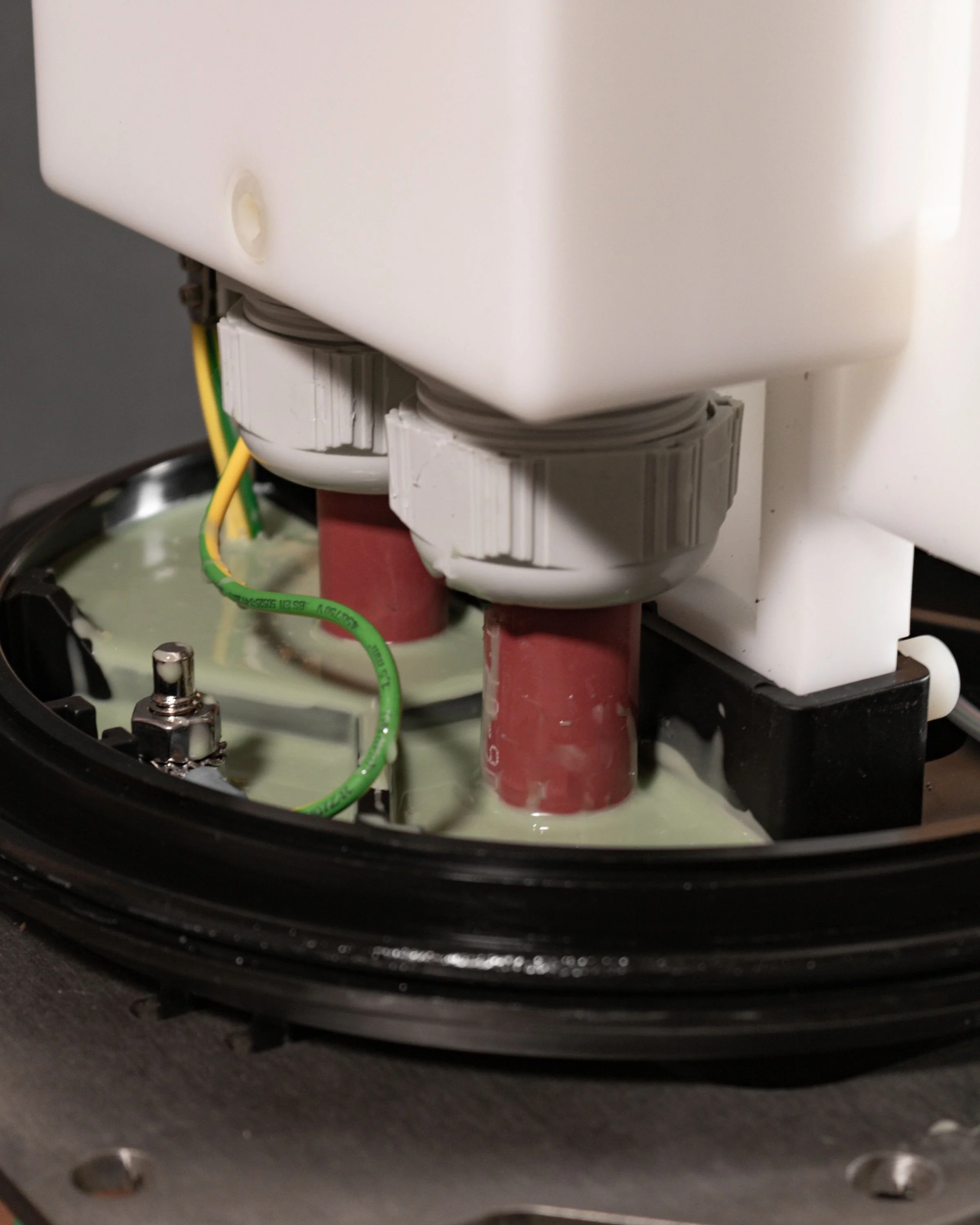 Close-up of a Universal Land Joint with white plastic components, red cylindrical parts, waterproofing resin surrounds green wires, and a black base.