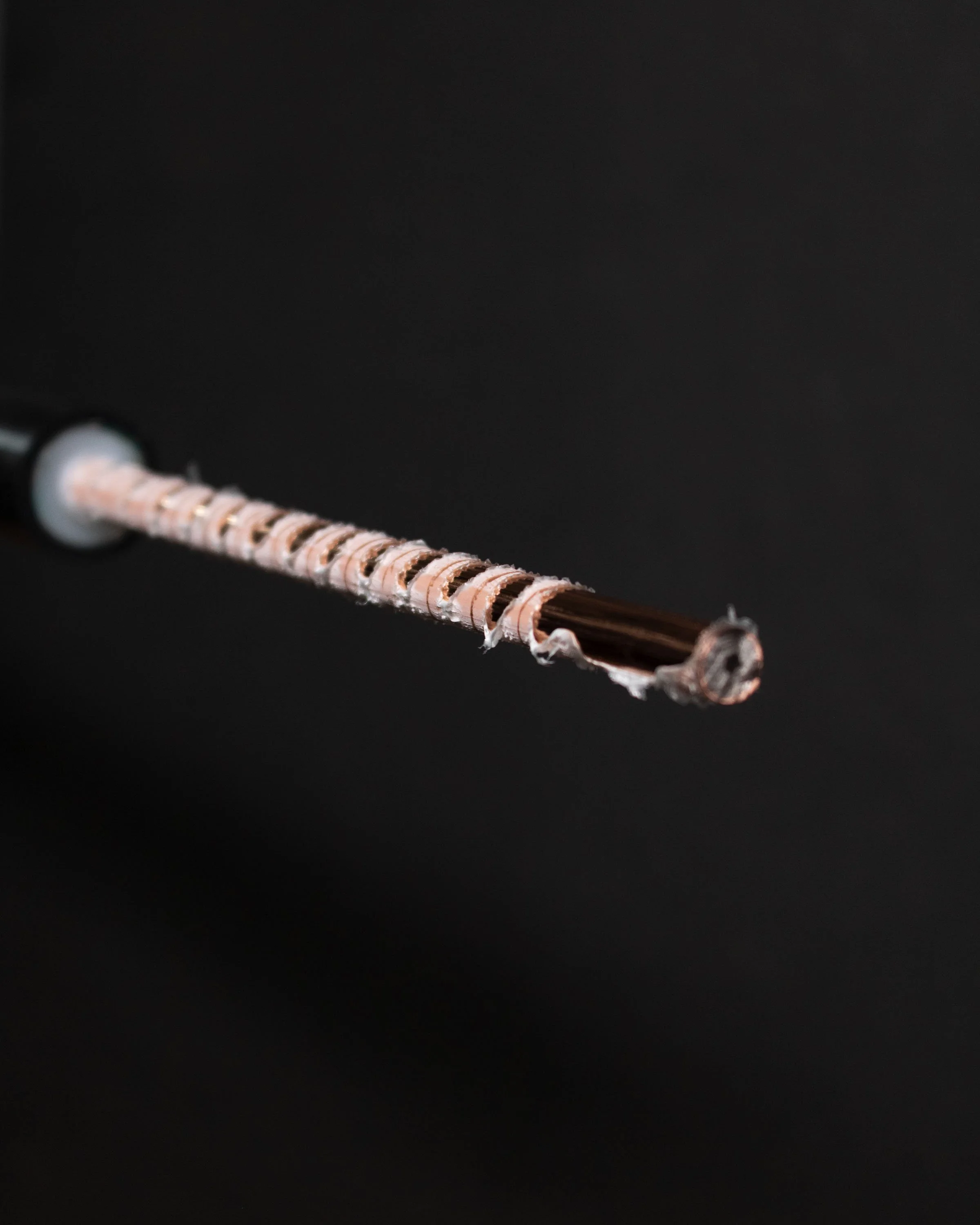 Close-up of a damaged wire with frayed copper strands on a dark background.