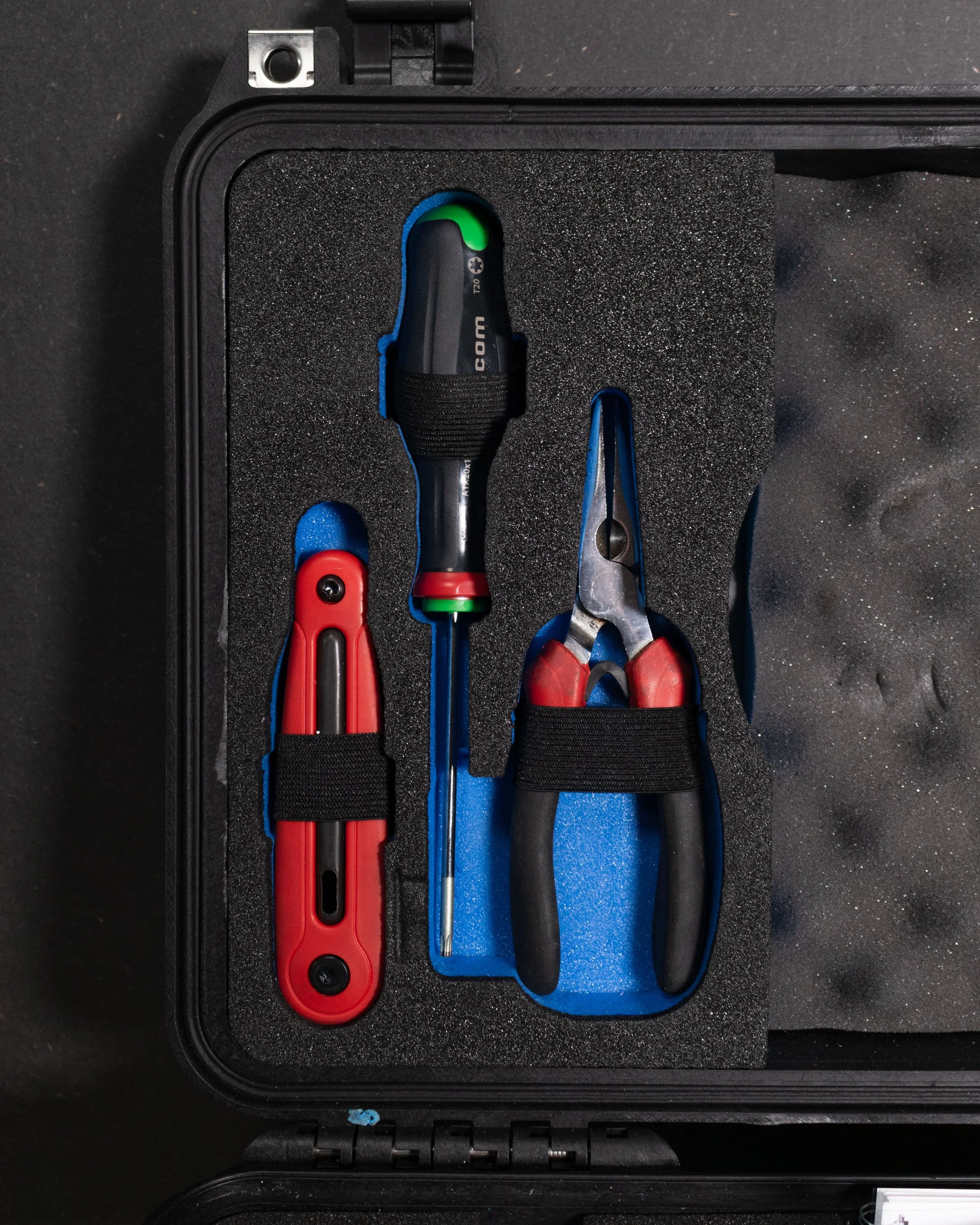 A black toolbox containing a screwdriver, a pair of pliers, and a wire stripper, all secured with black elastic straps.