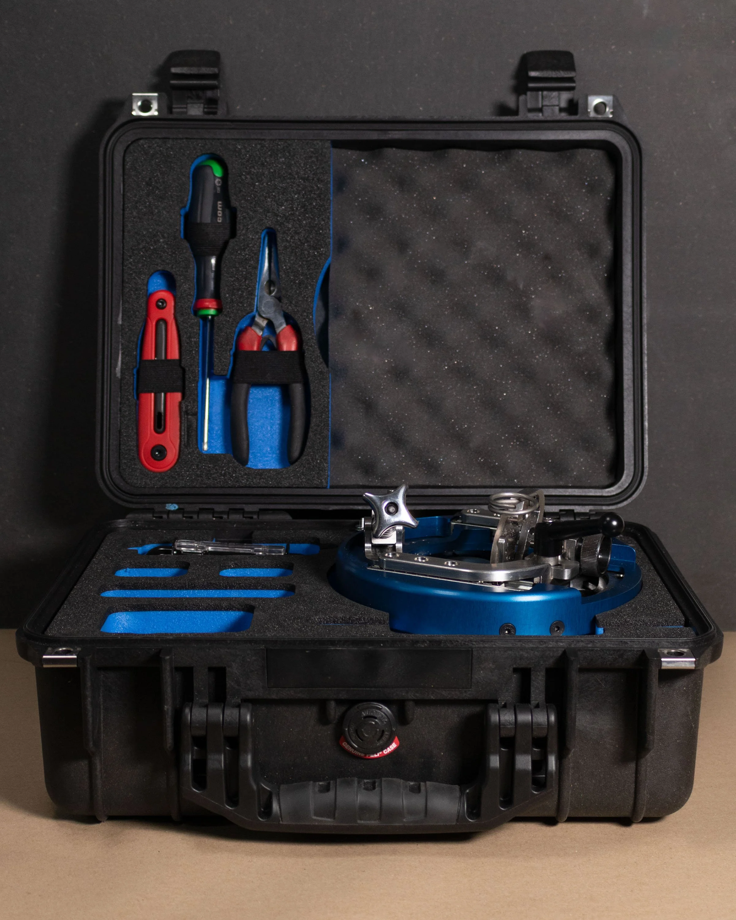 An open black protective case containing a blue surgical instrument, a pair of pliers, a screwdriver, and other small tools