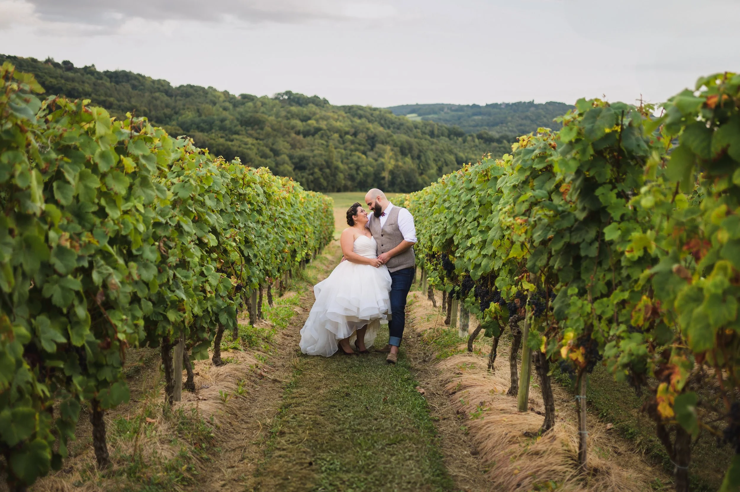 A bride and groom walking hand in hand through a vineyard, smiling and enjoying each other's company.