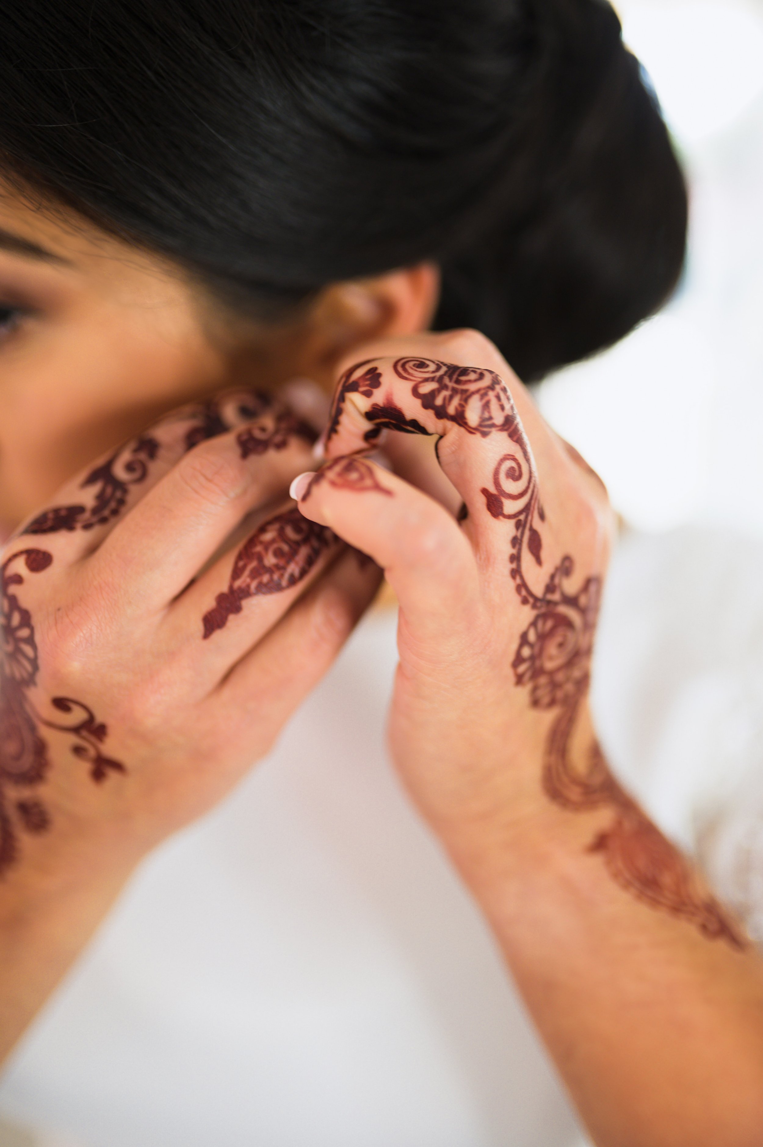 Close-up of a woman with black hair and henna designs on her hands and fingers as she adjusts her earring.