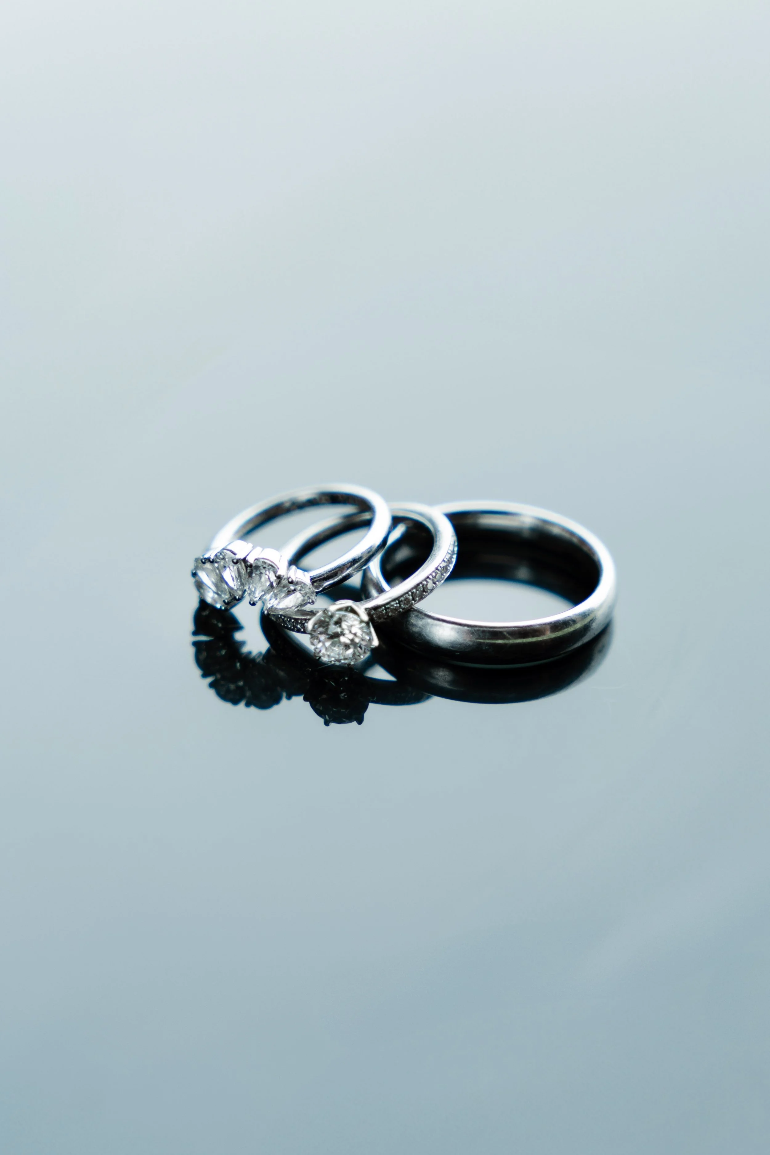 Three silver rings with diamonds on a reflective black surface.
