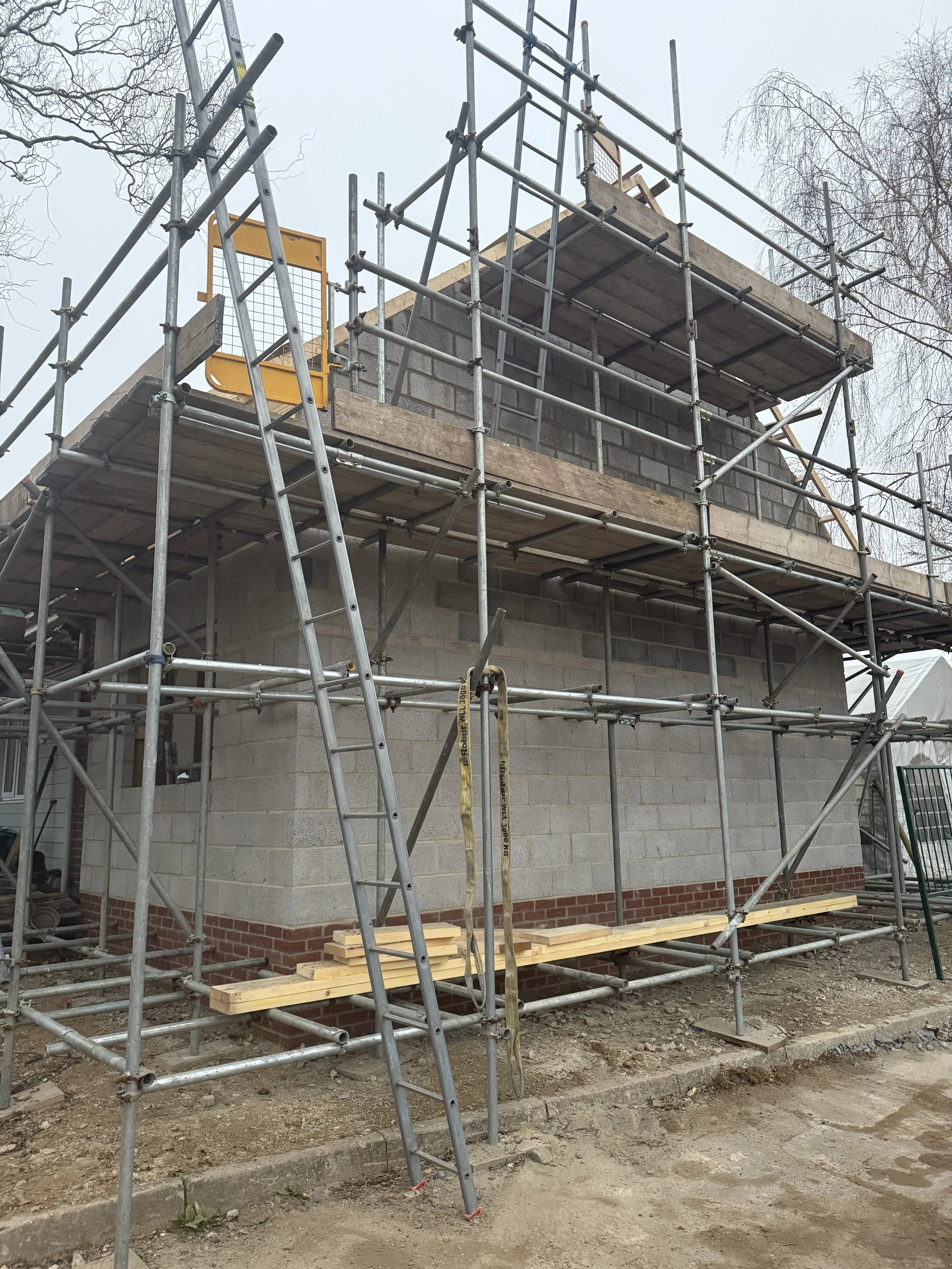 Under construction house with scaffolding around it, showing brick and concrete block walls, and a ladder leaning on the scaffolding.
