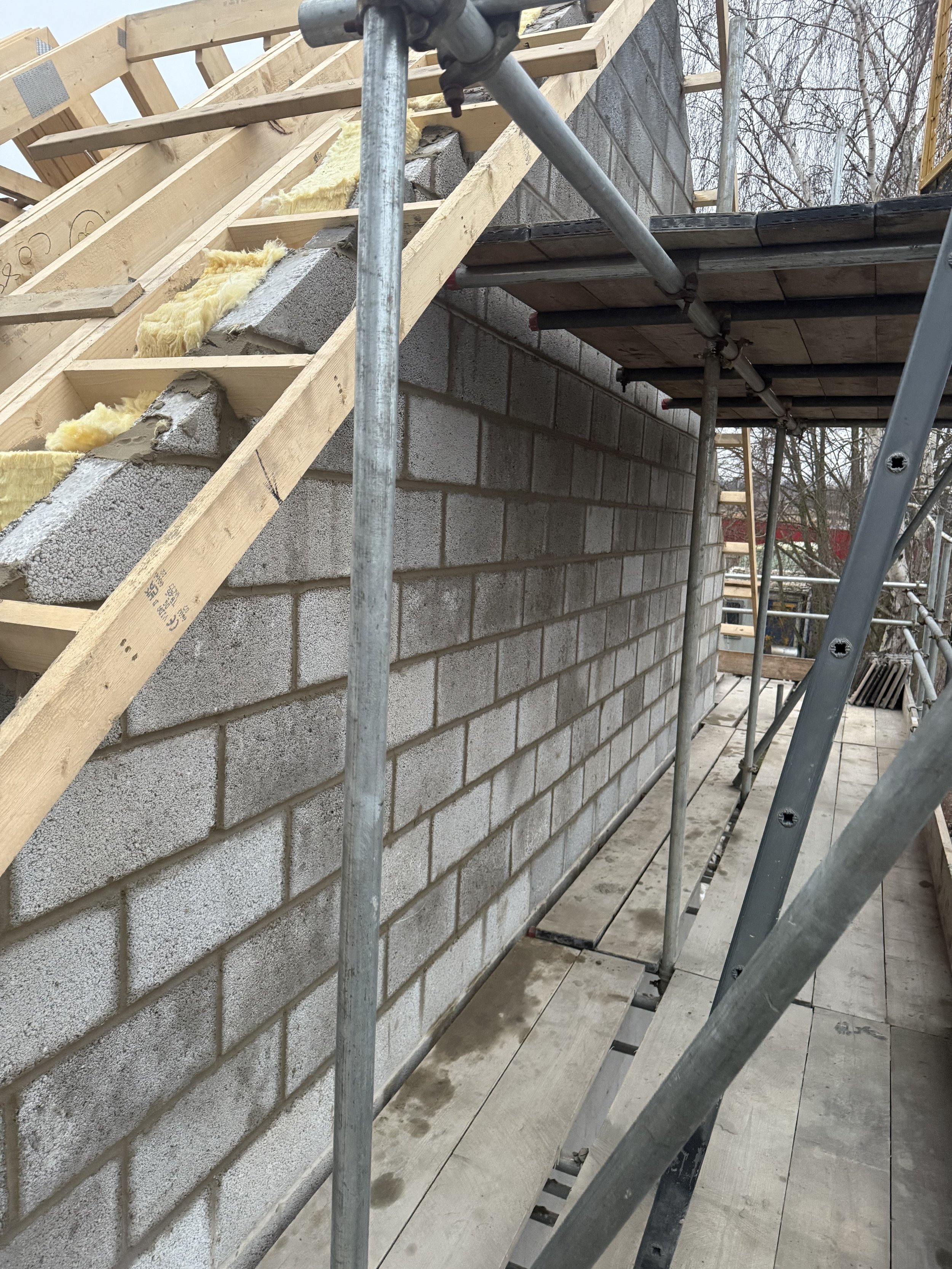 Construction scaffolding with brick wall and wooden stairs in progress, with insulation material visible.