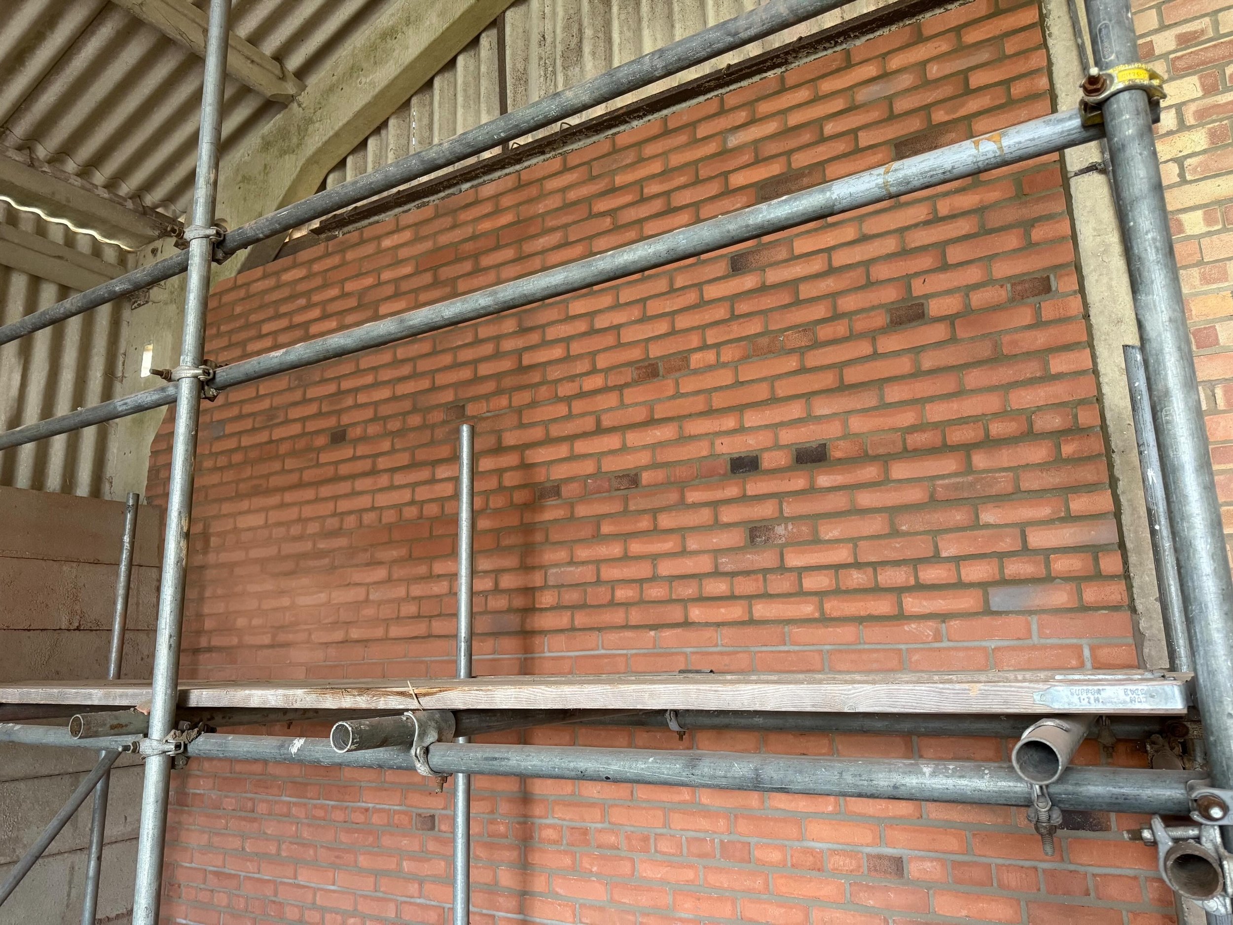 Construction scaffolding set up against a brick wall inside a building under construction.
