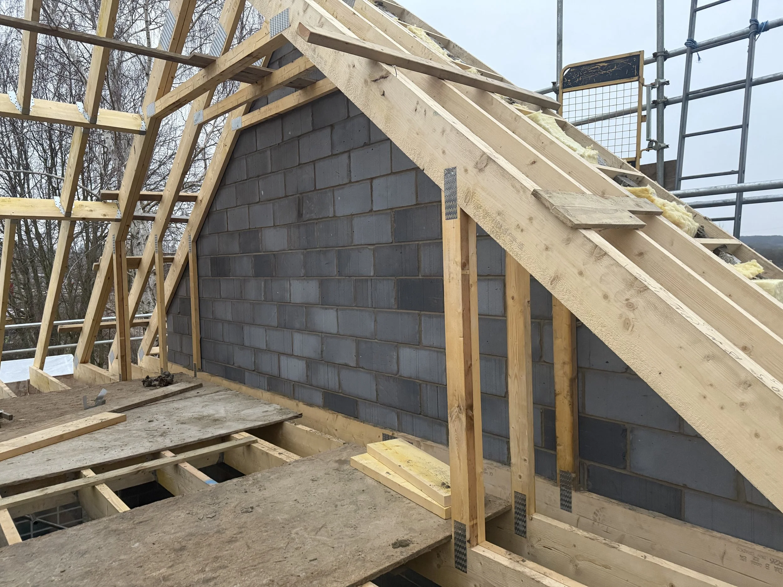 Construction site of a house roof with wooden framing and a brick chimney on a cloudy day.