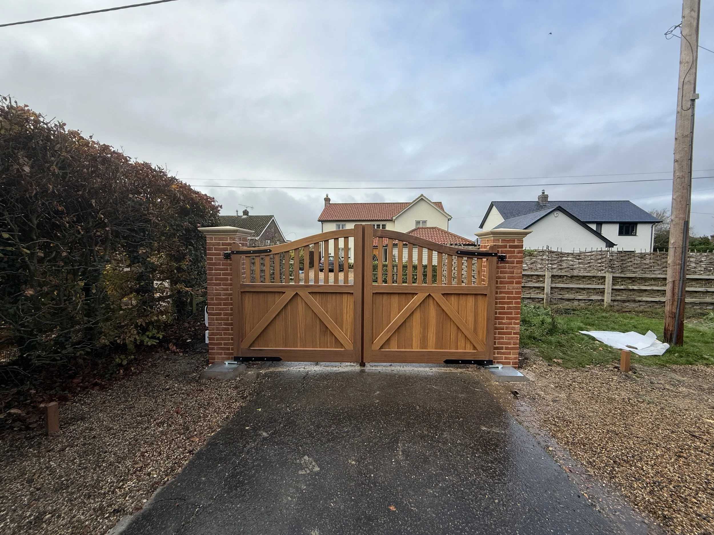 A wooden gate with brick pillars on each side, situated at the entrance of a driveway.
