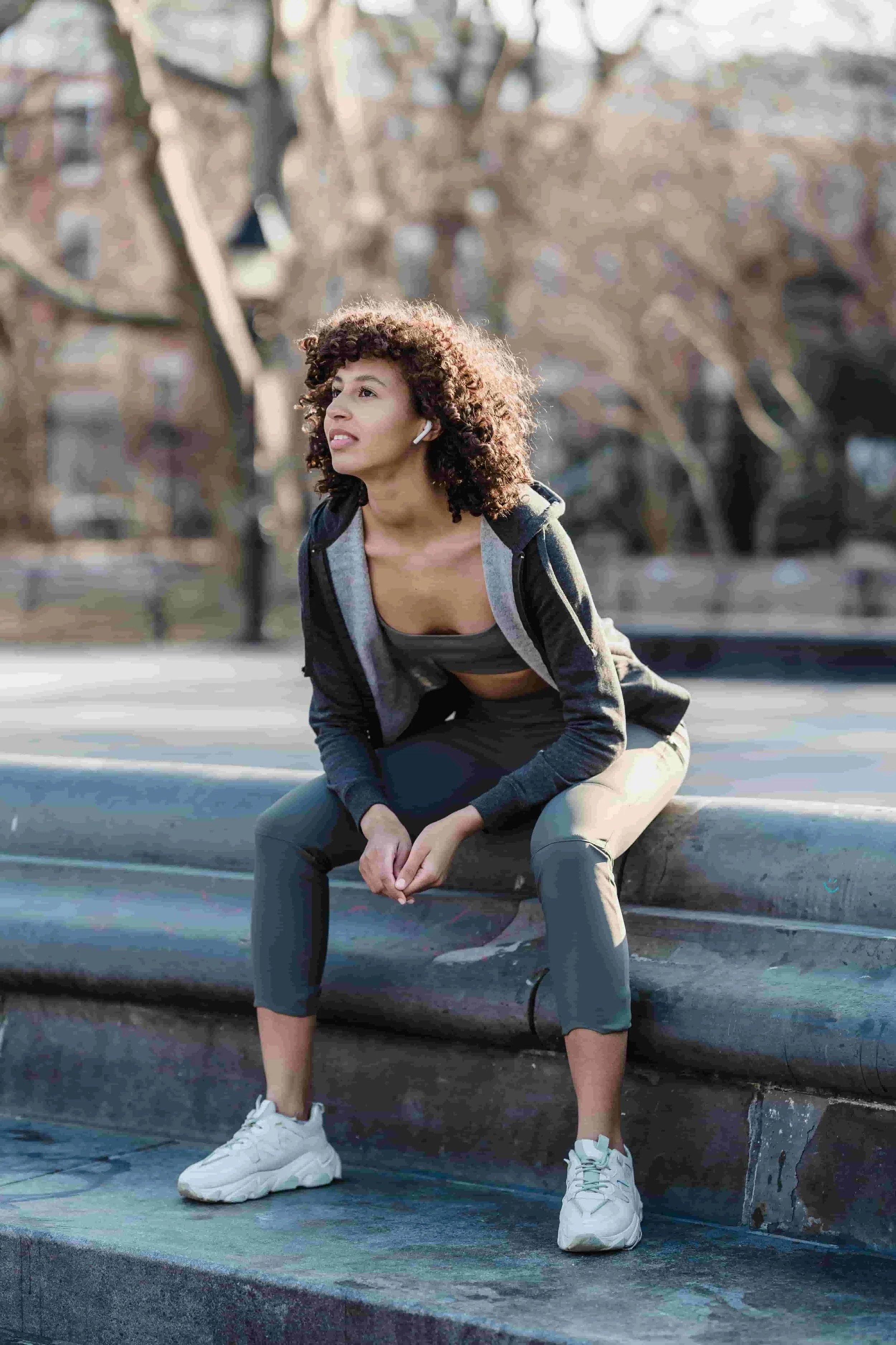 A woman runner sitting in a calm post-run pause, looking outward, grounded and steady.